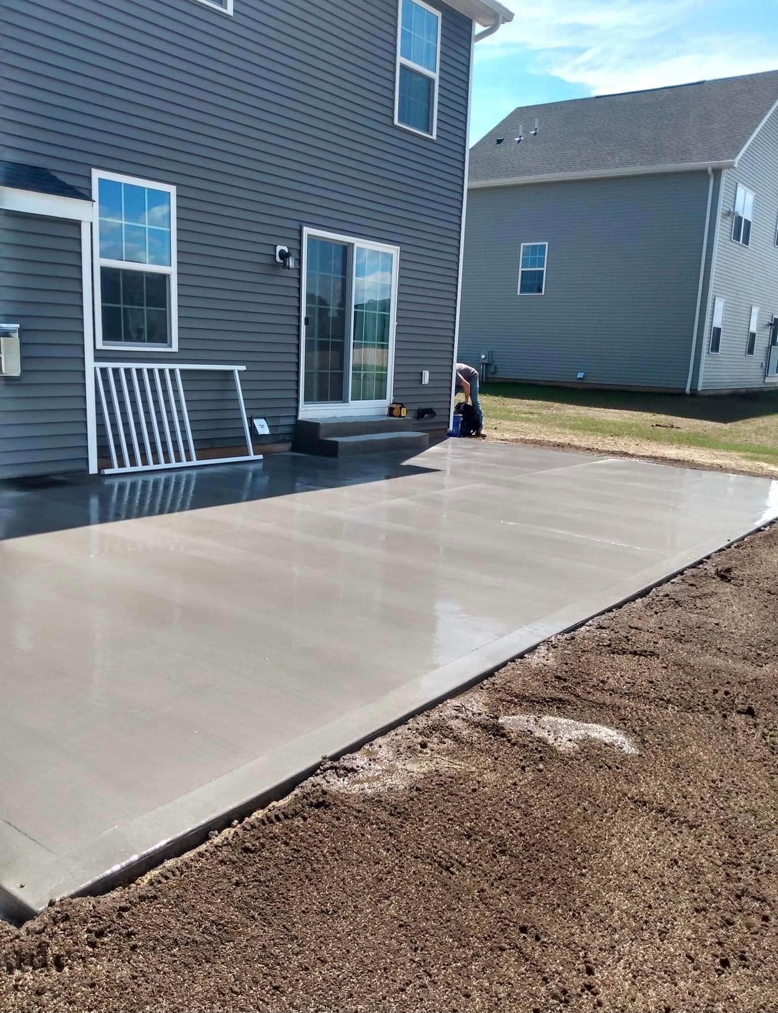 Freshly poured concrete patio extending from back of gray house