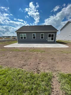 Newly constructed gray ranch home with wide backyard and dramatic sky