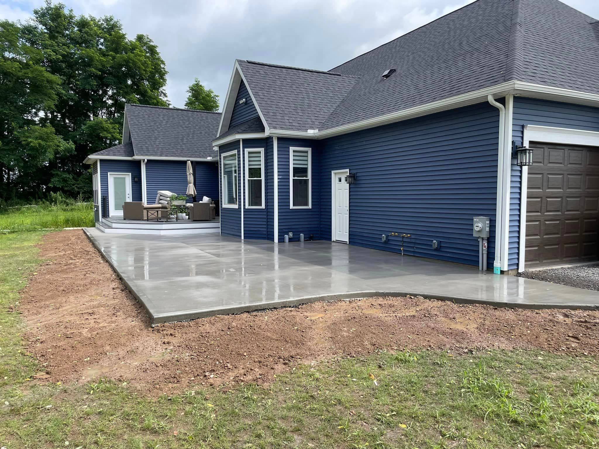 Freshly poured concrete patio and driveway at blue house with garage
