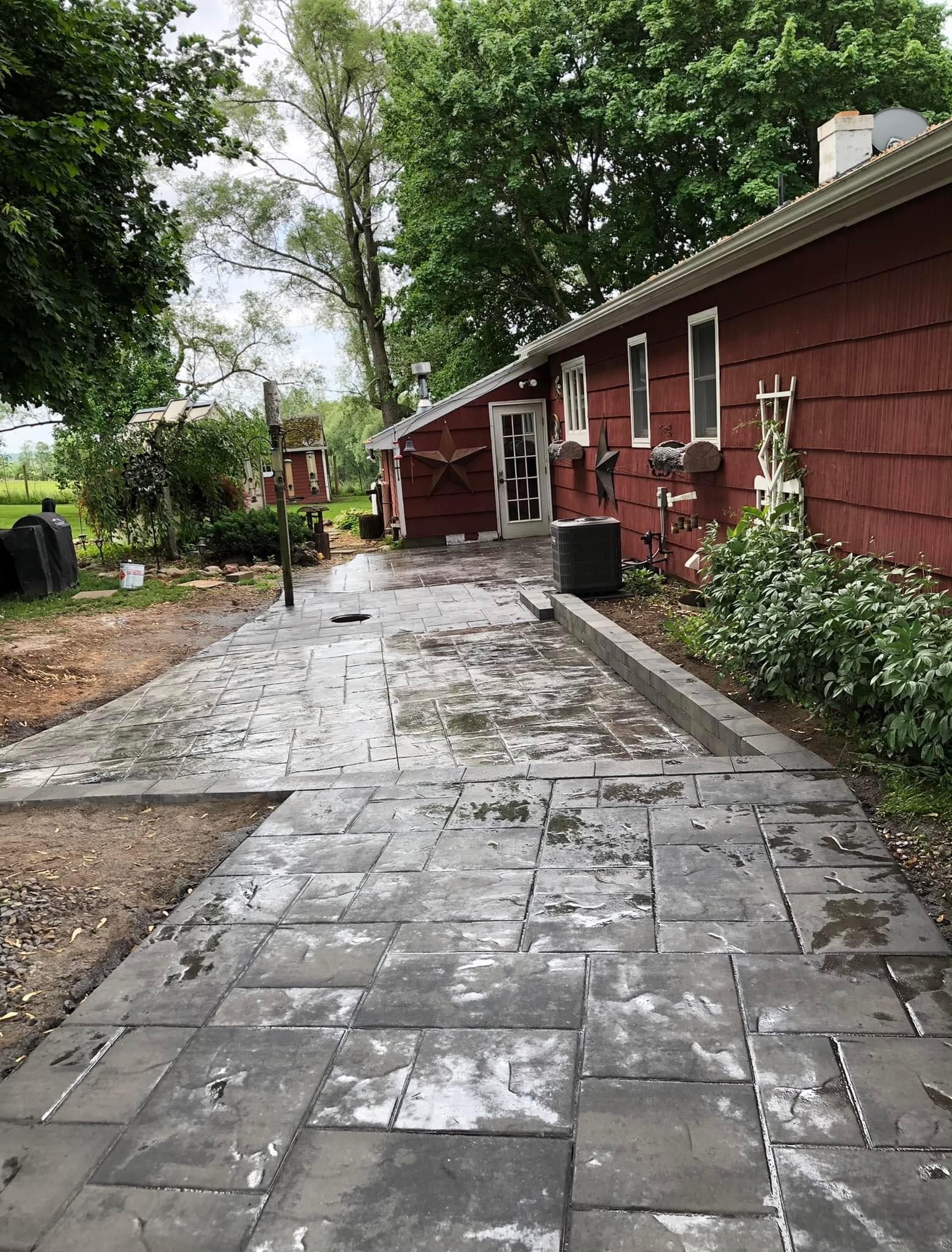 Wet paver patio and walkway leading to red barn building with white trim