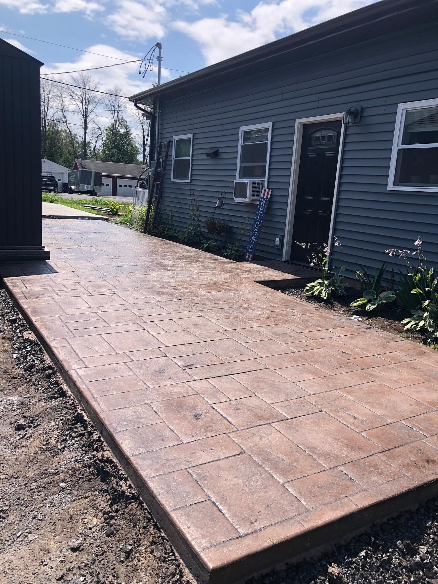 Tan paver patio with stepped border beside gray house with door