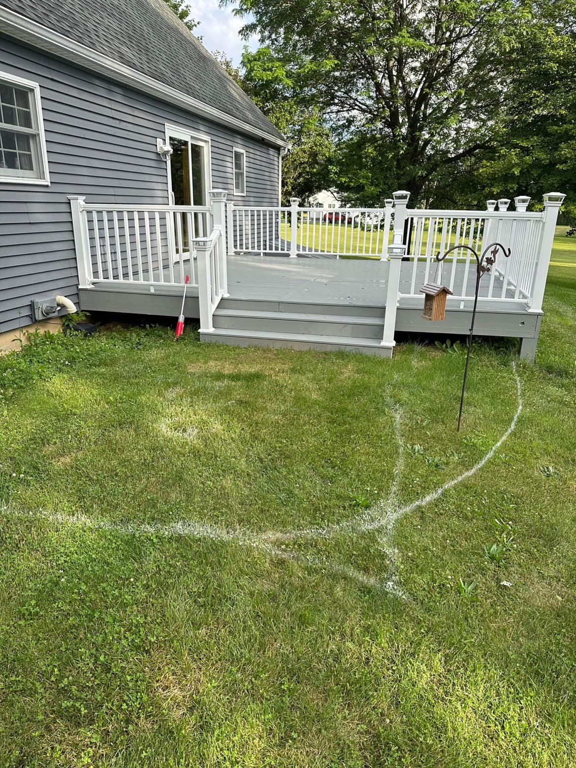 White spray paint markings on lawn outlining concrete work area near gray deck