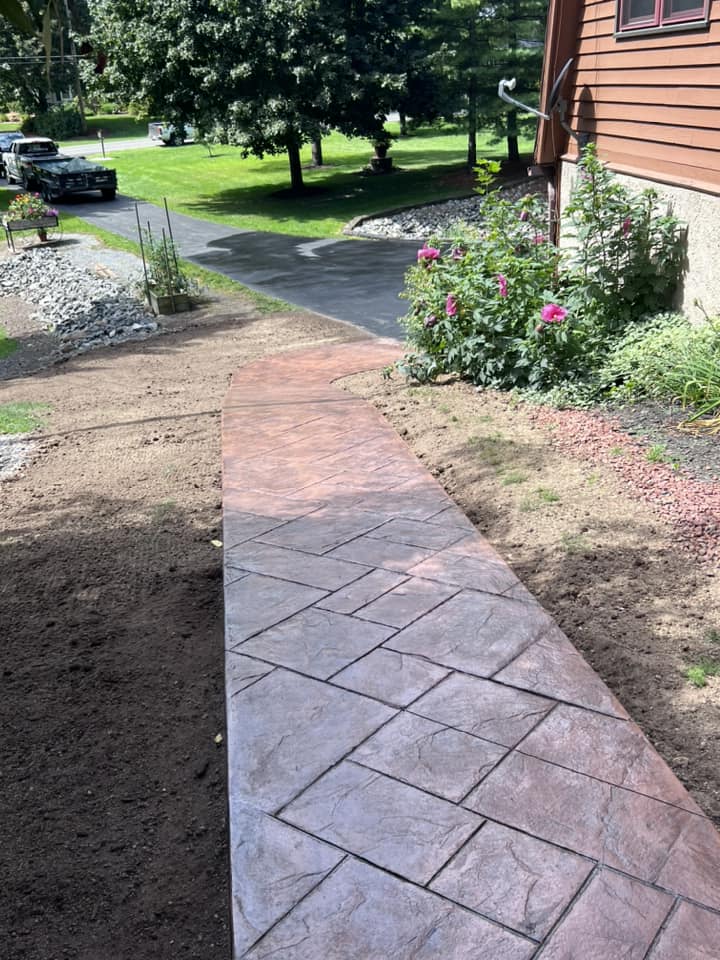 Curved stamped concrete walkway leading to orange house with garden beds