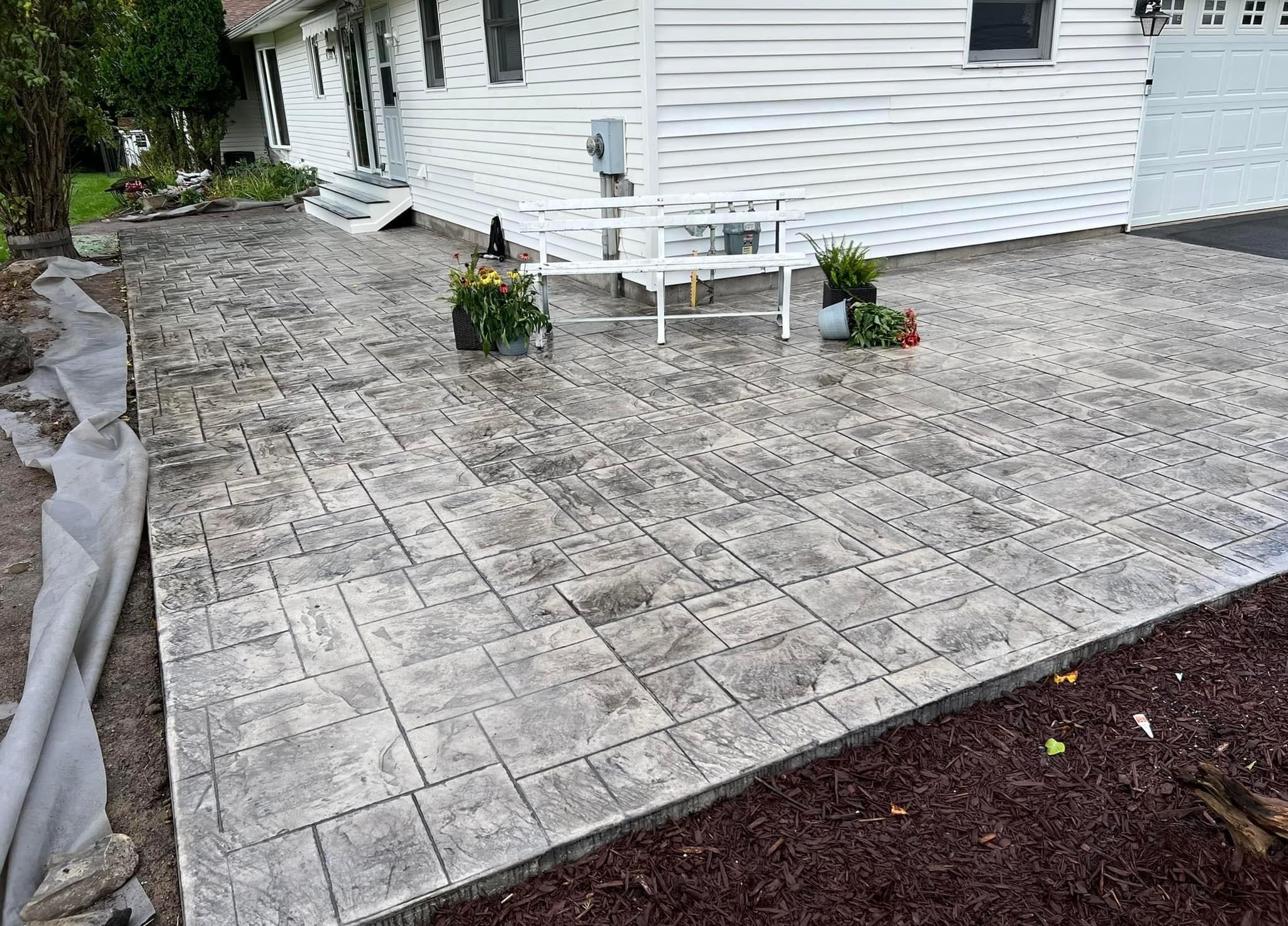 Large stamped concrete patio with decorative pattern next to white house