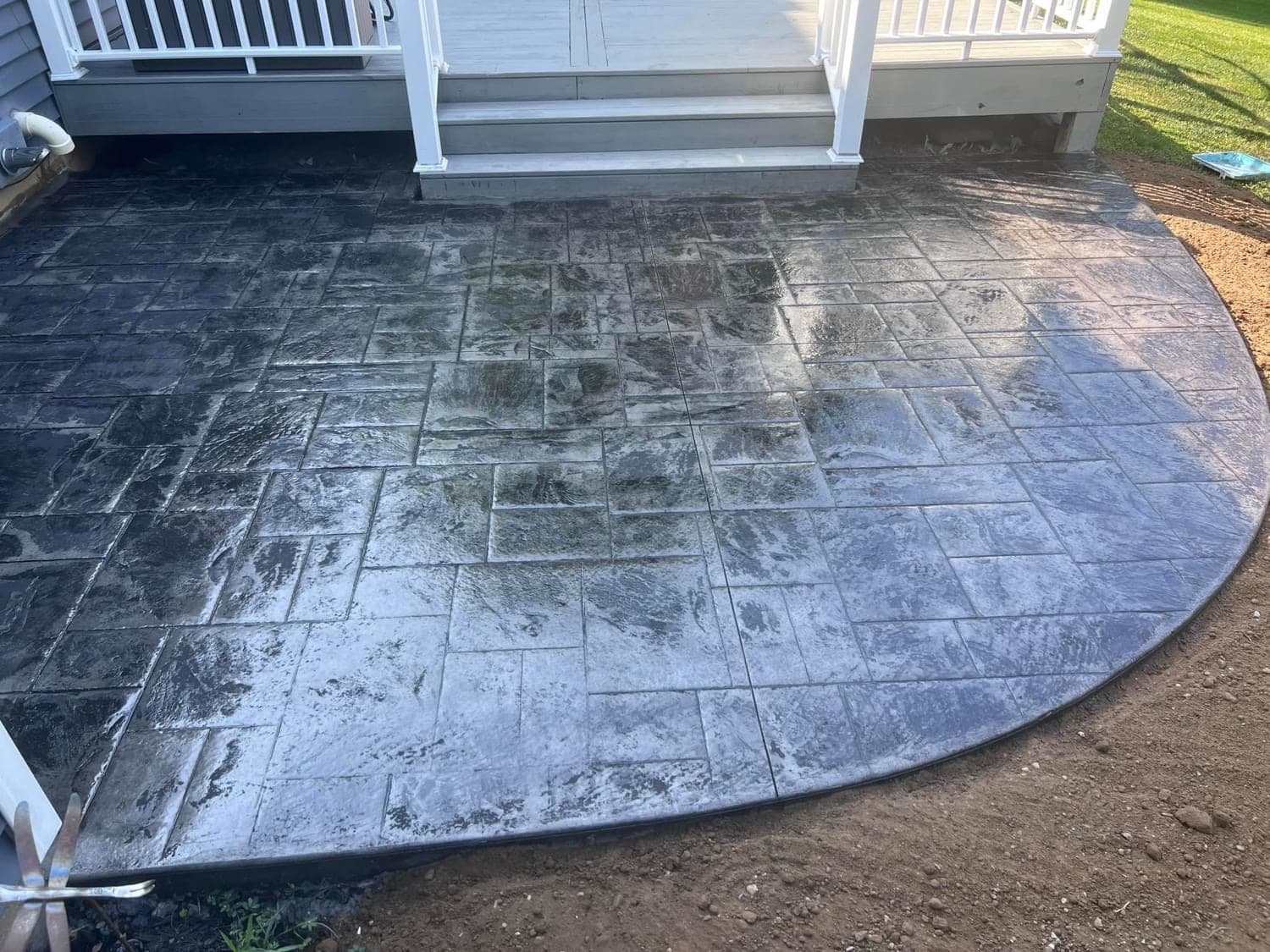 Stamped concrete patio with ashlar slate pattern below white deck stairs