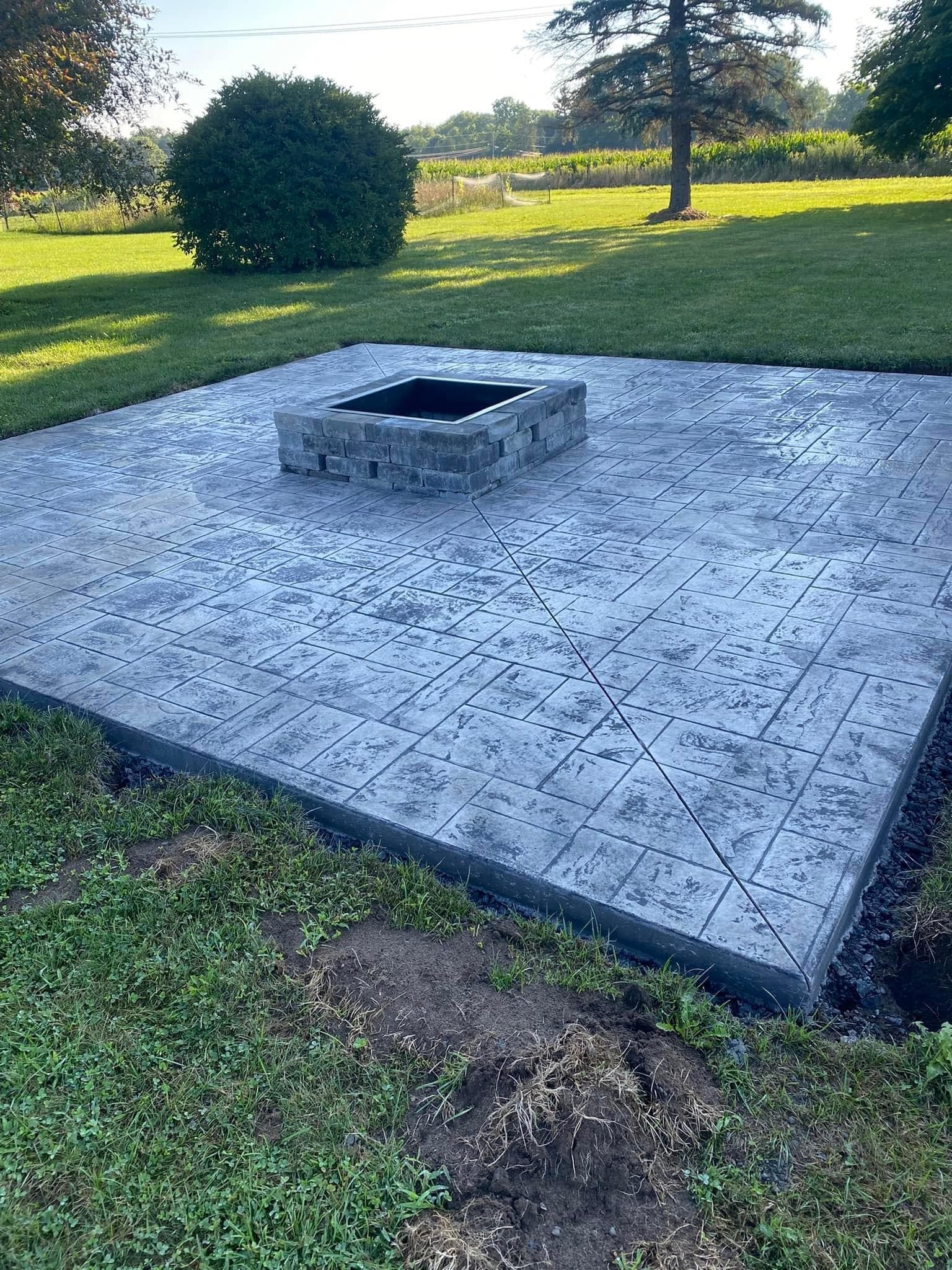 Gray stamped concrete patio with square stone fire pit in backyard