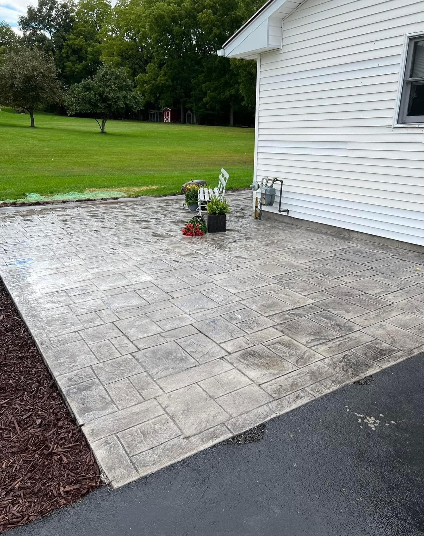 Stamped concrete patio extending from white house with planters and lawn