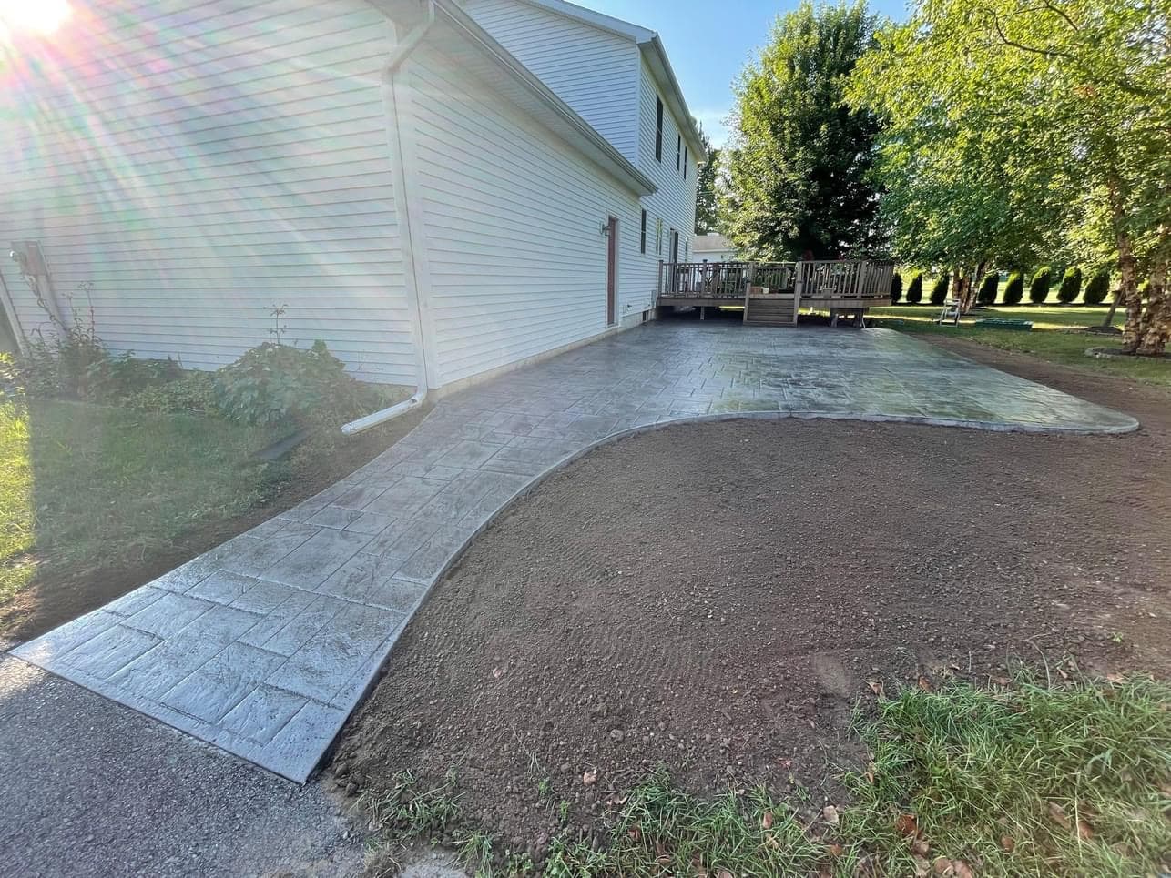 Freshly installed stamped concrete patio beside house with wooden deck