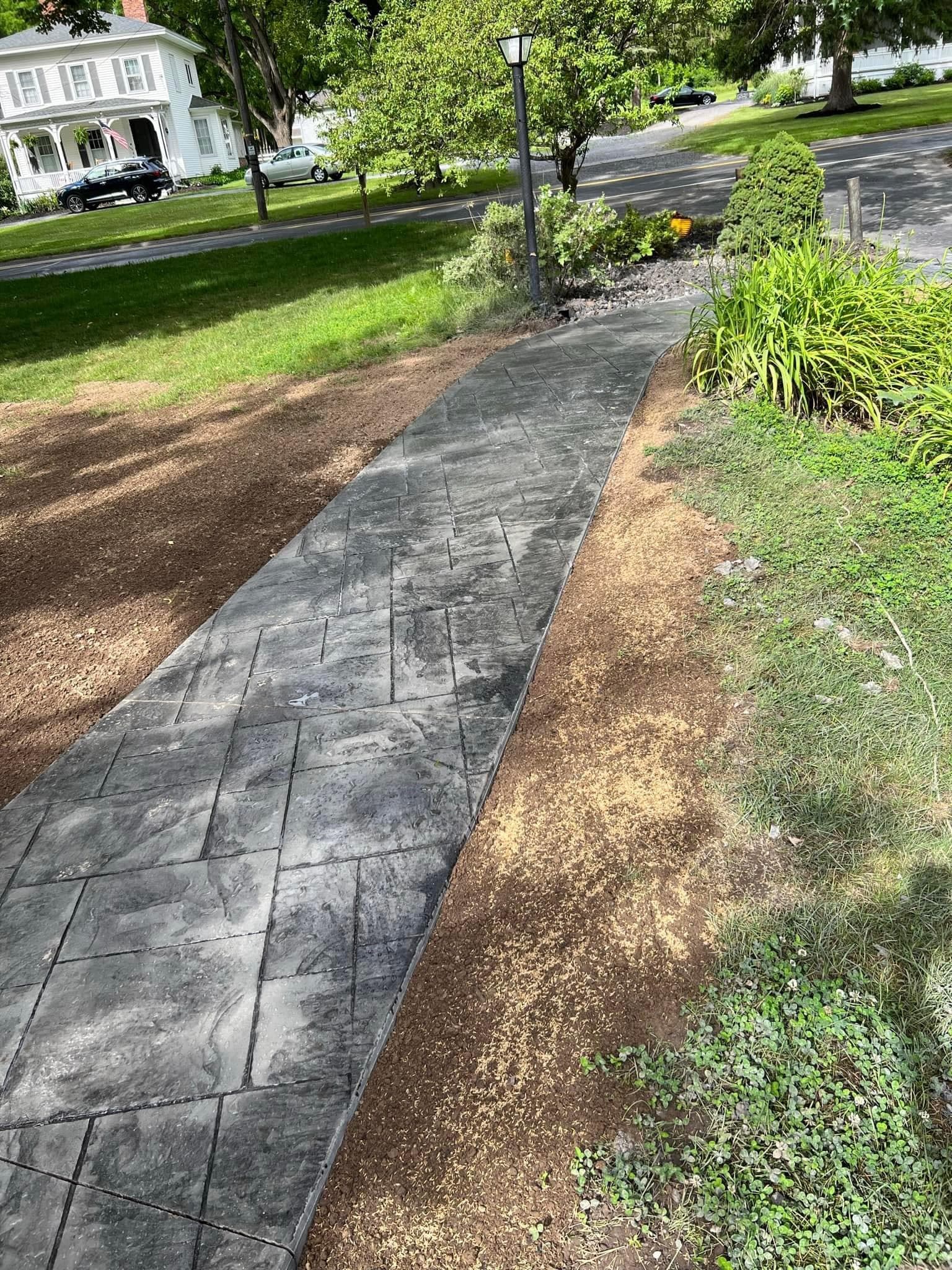 Stamped concrete walkway bordered by fresh dirt and landscaping near residential street