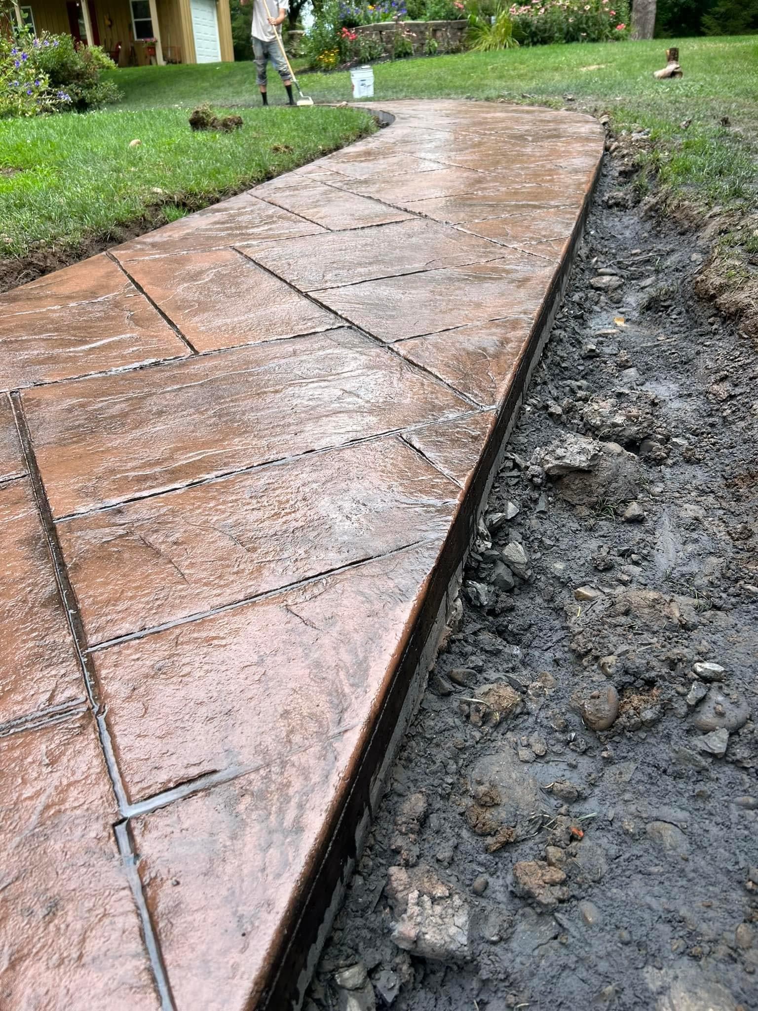 Stamped concrete walkway under construction with exposed dirt edge and green lawn