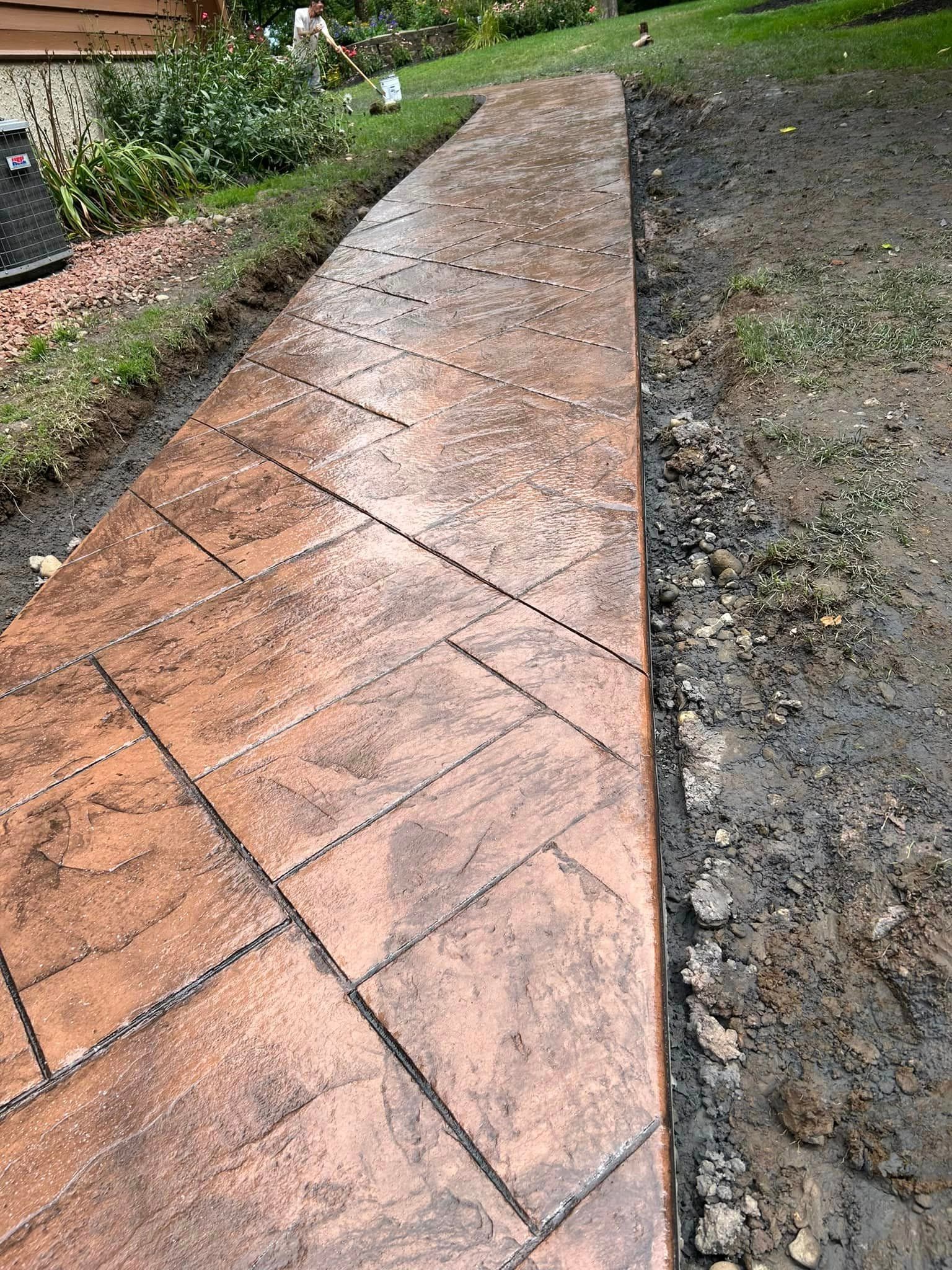 Stamped concrete walkway with wood plank pattern bordered by dirt and grass