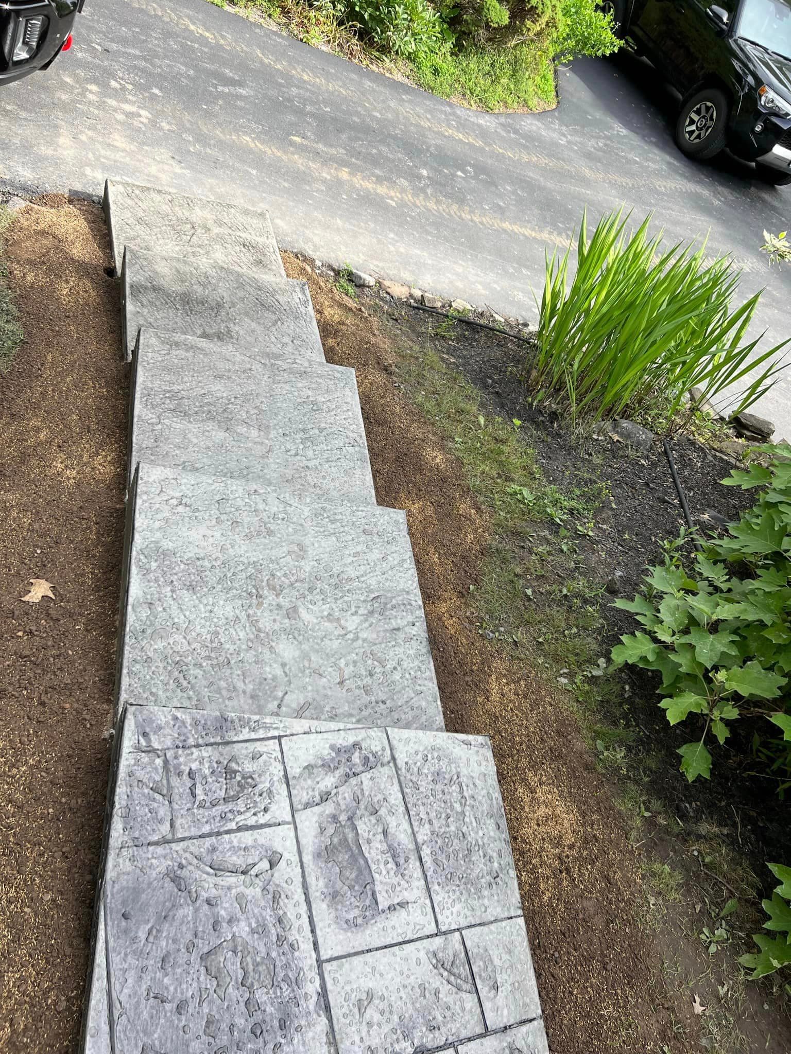 New stamped concrete walkway and steps leading to driveway with landscaping