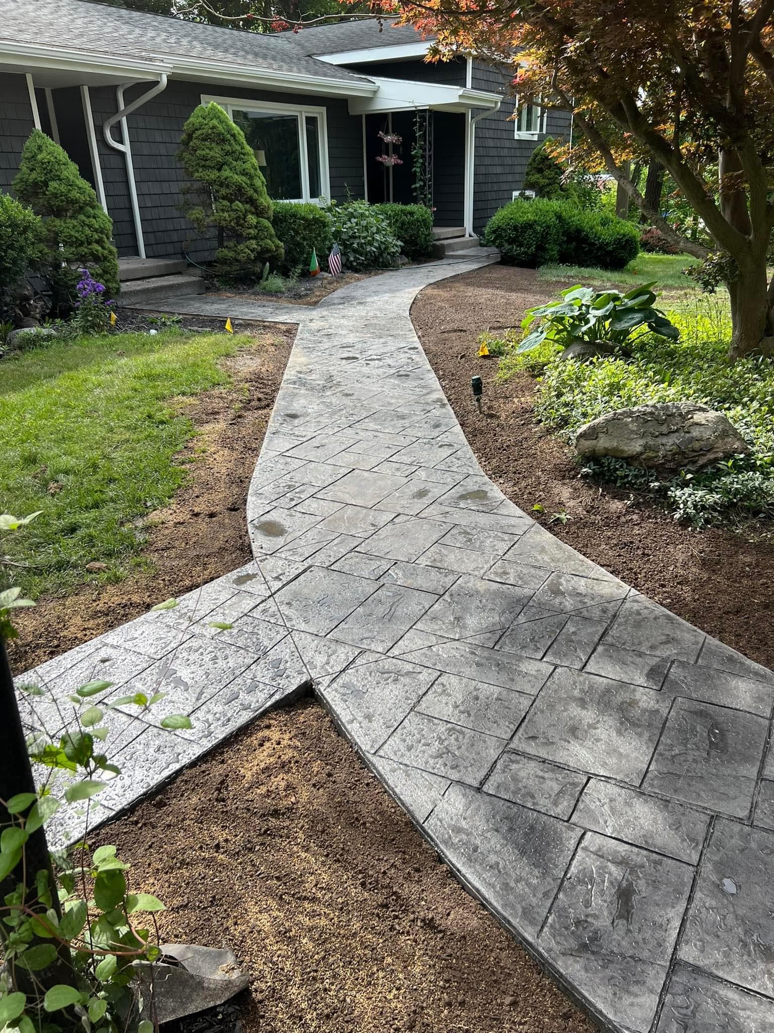 Curved stamped concrete walkway leading to house entrance with landscaping