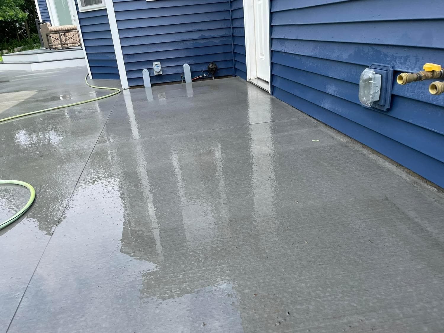 Freshly poured concrete deck with wet surface between blue-sided houses