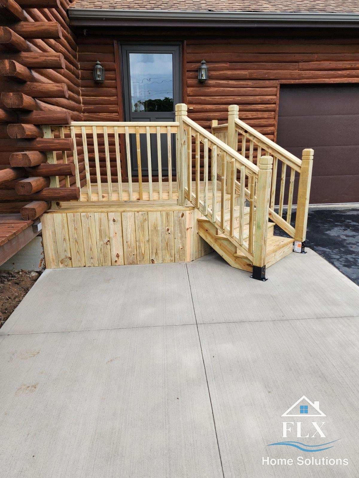 New wooden deck stairs and railing at log cabin entrance with concrete pad