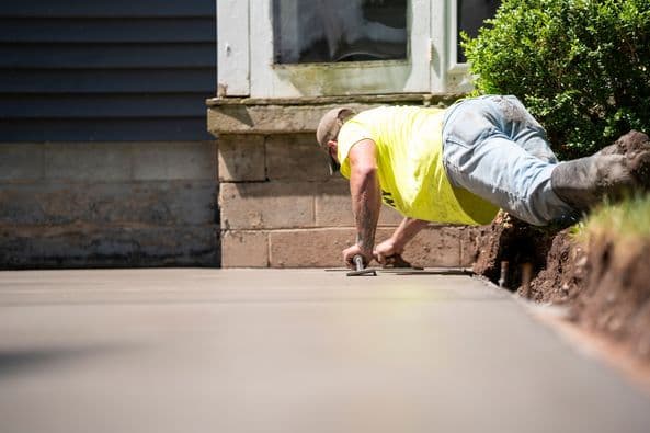 Construction worker in yellow shirt smoothing freshly poured concrete surface
