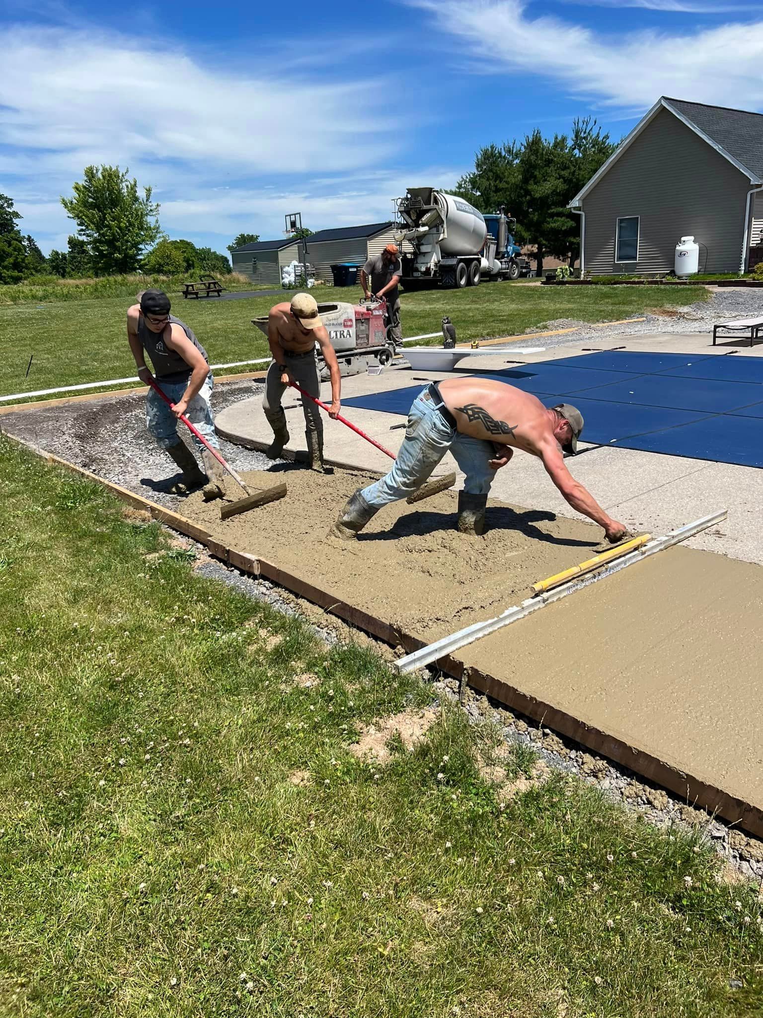Three workers using red pull screeds to smooth wet concrete slab