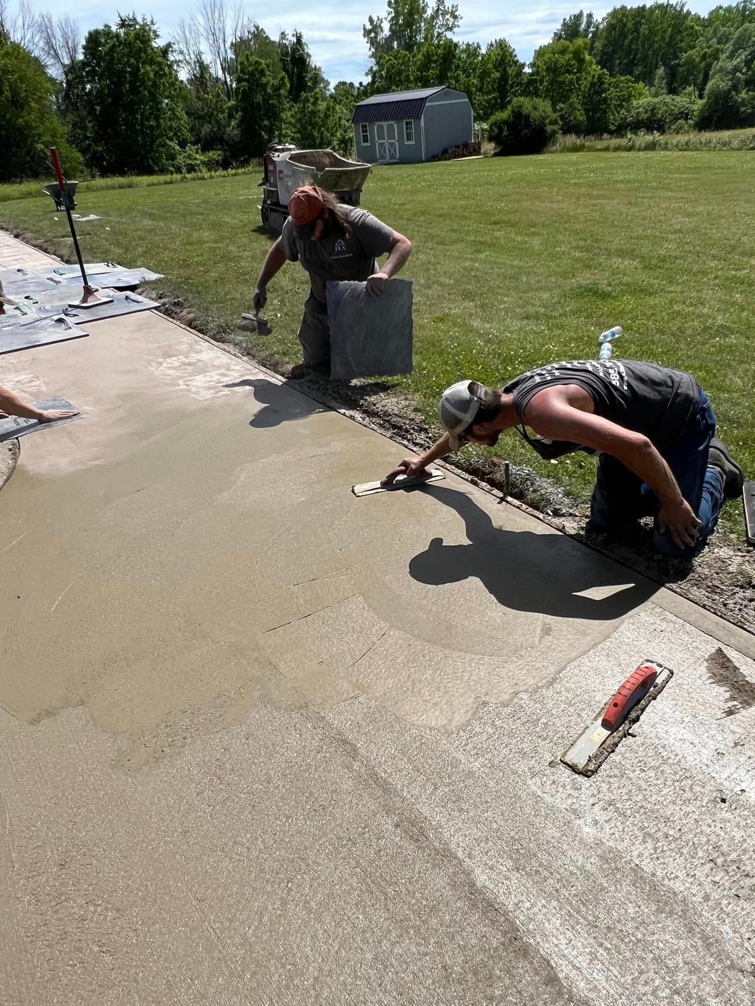 Two workers smoothing and finishing a freshly poured concrete walkway