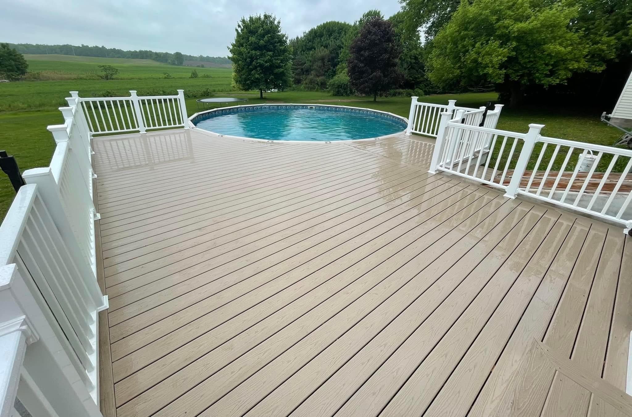 Composite deck with white railings surrounding above-ground pool overlooking fields