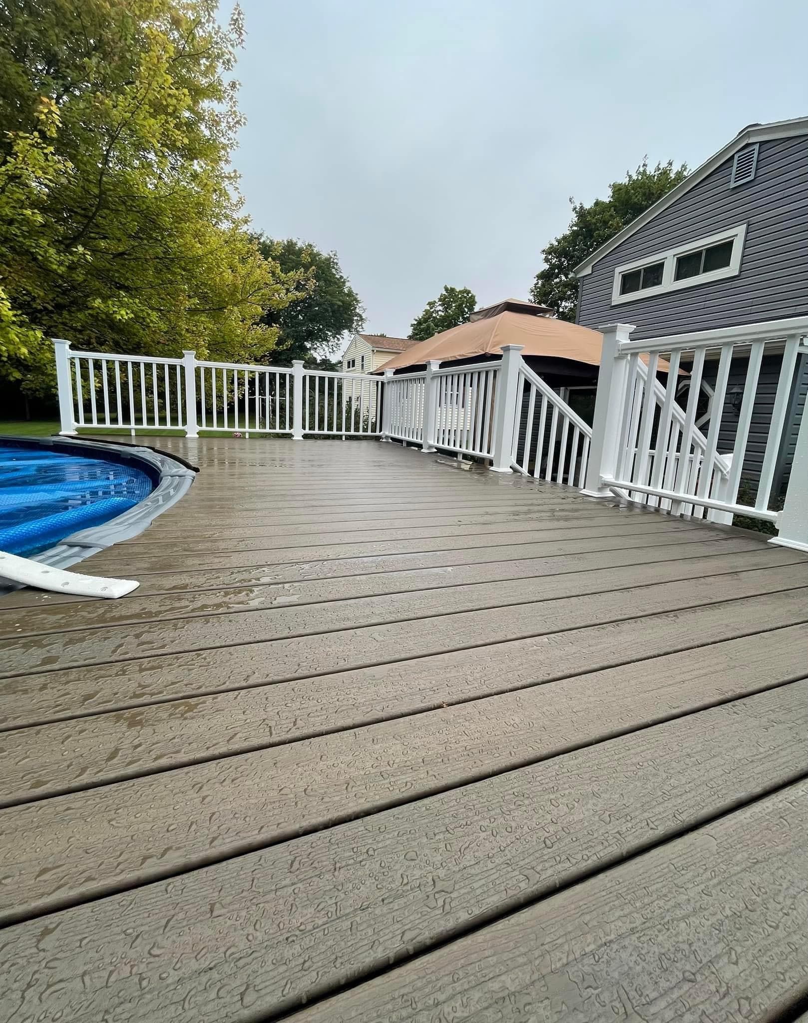 Composite deck with white railing surrounding above-ground pool in backyard