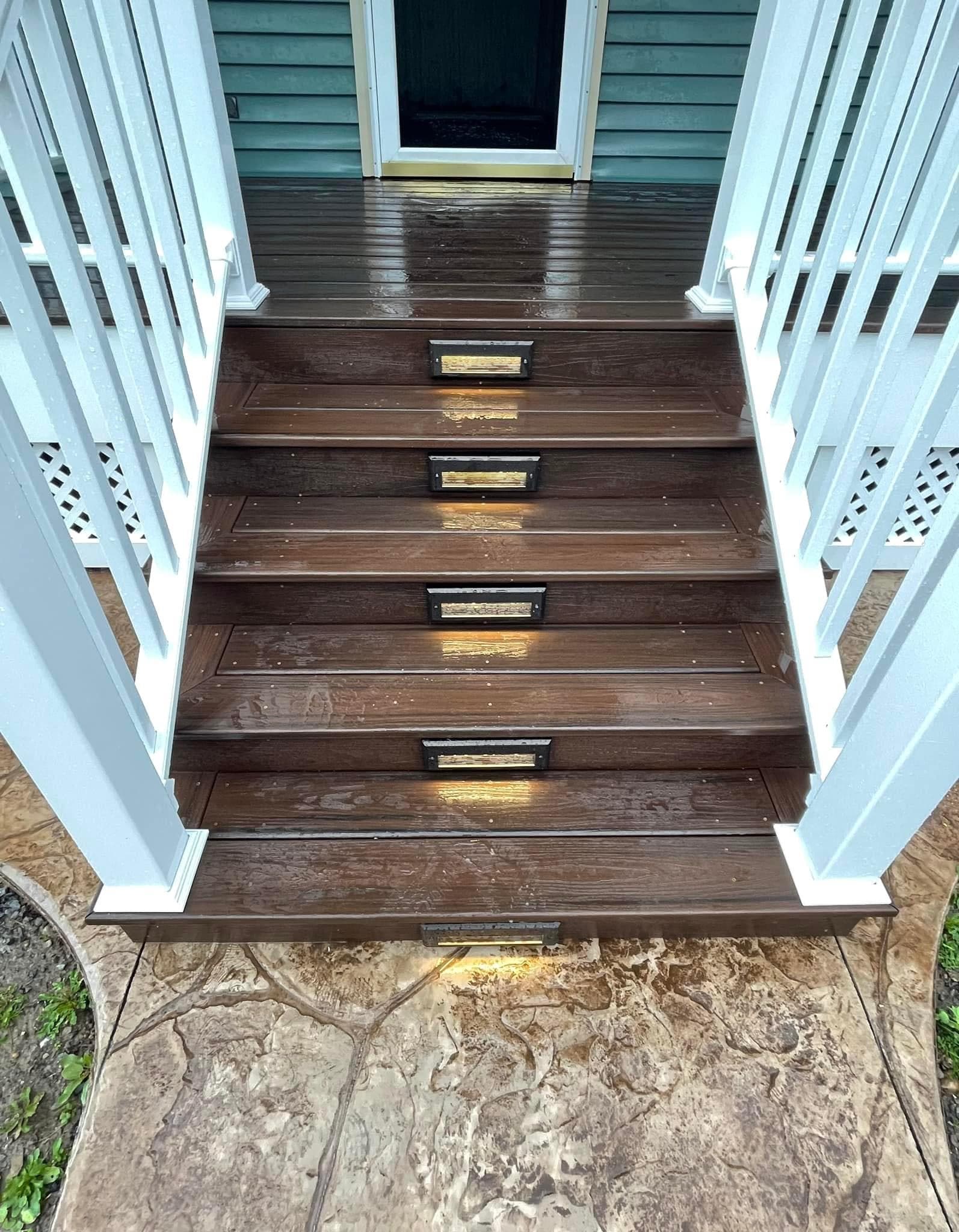 Dark stained wood deck stairs with white railings and integrated step lighting
