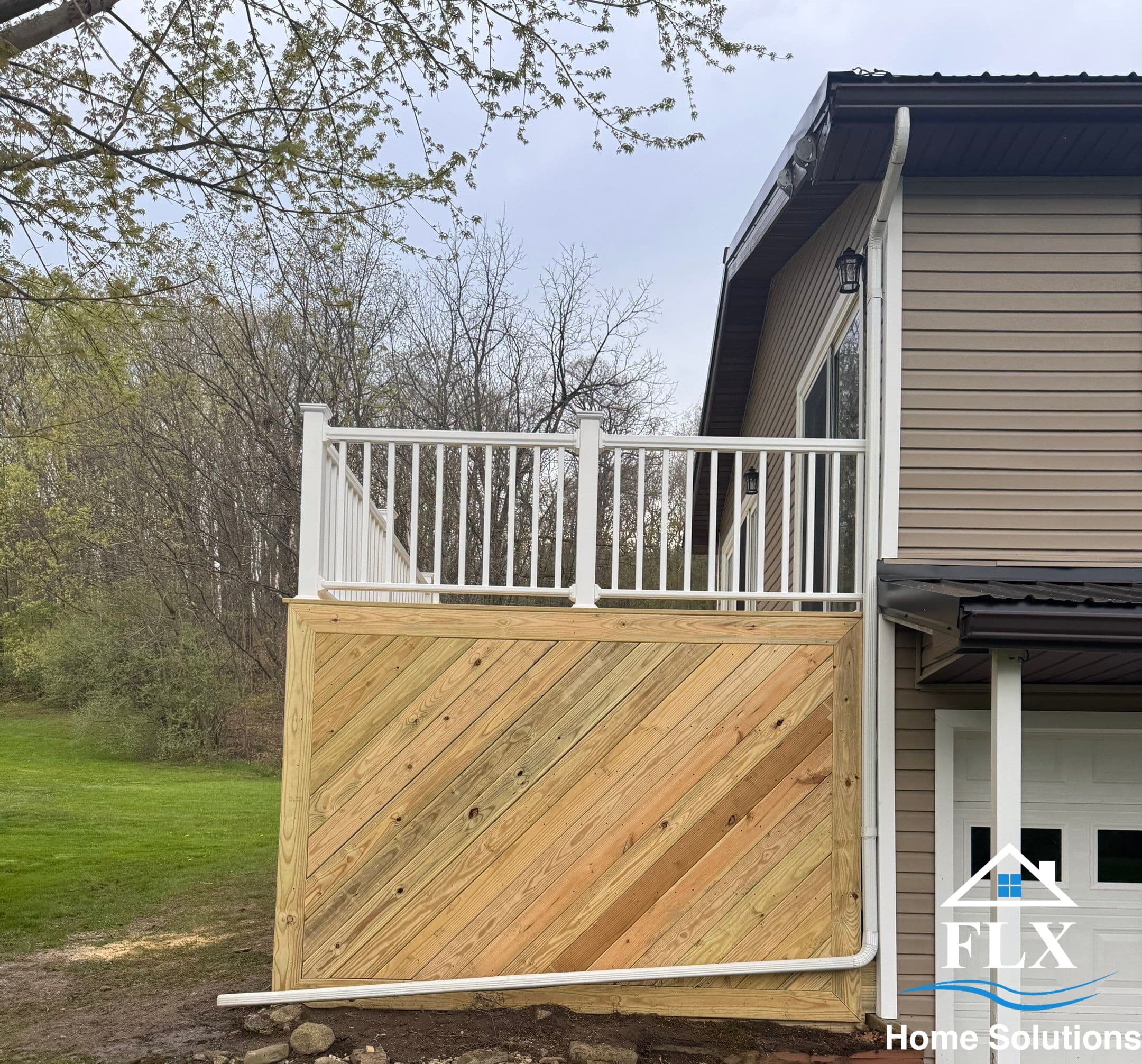 Elevated deck with white railing and diagonal wood skirting on beige house