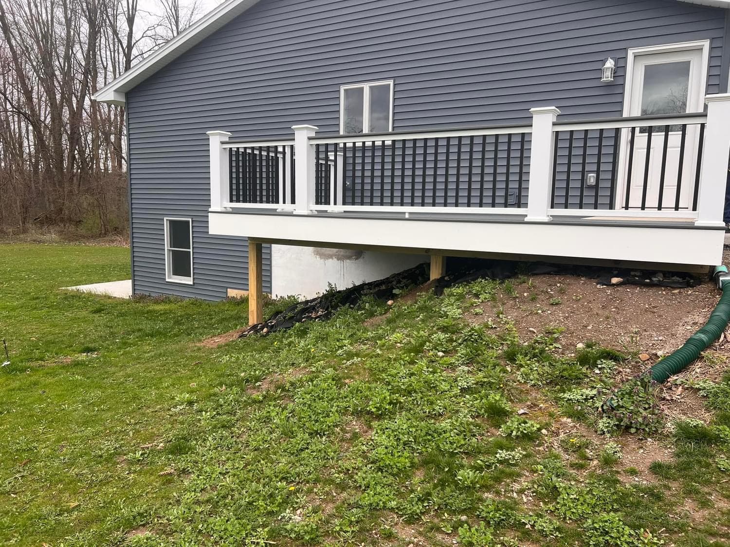 Gray house with elevated white deck supported by wooden posts, foundation work in progress