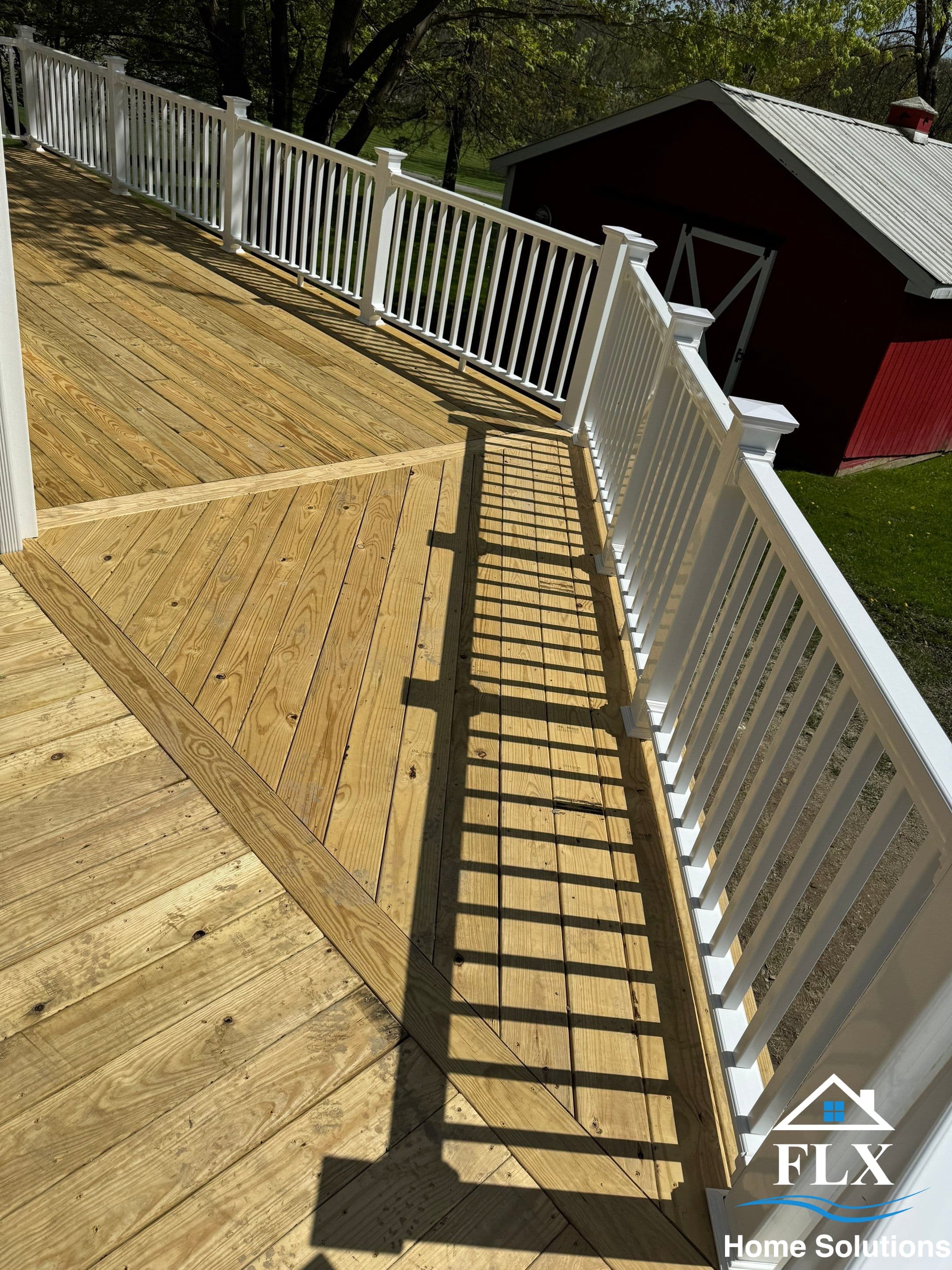 Elevated wooden deck with white vertical railings and red barn in background