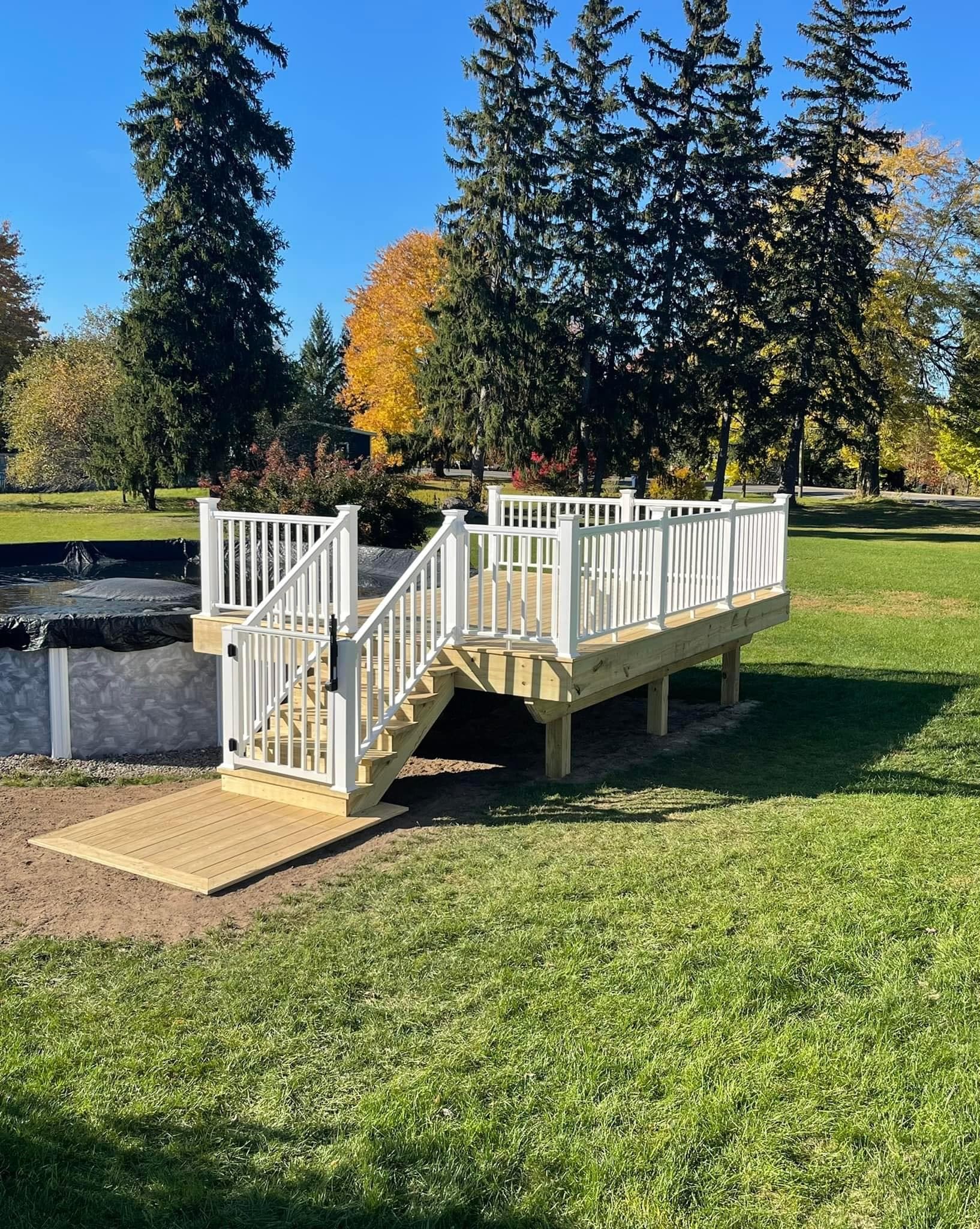 Elevated wooden deck with white railings and gate next to above-ground pool