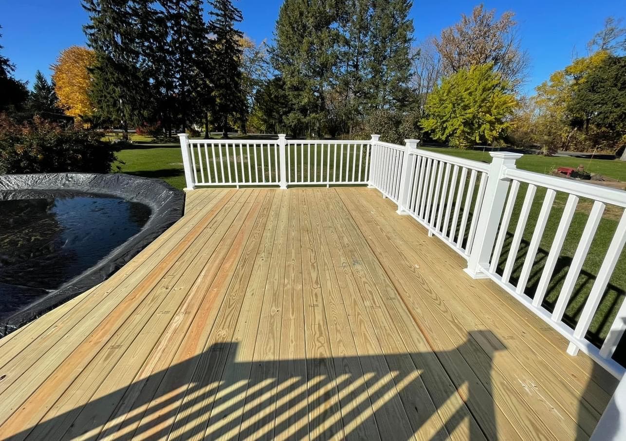 Natural wood deck with white vertical railing overlooking park with trees