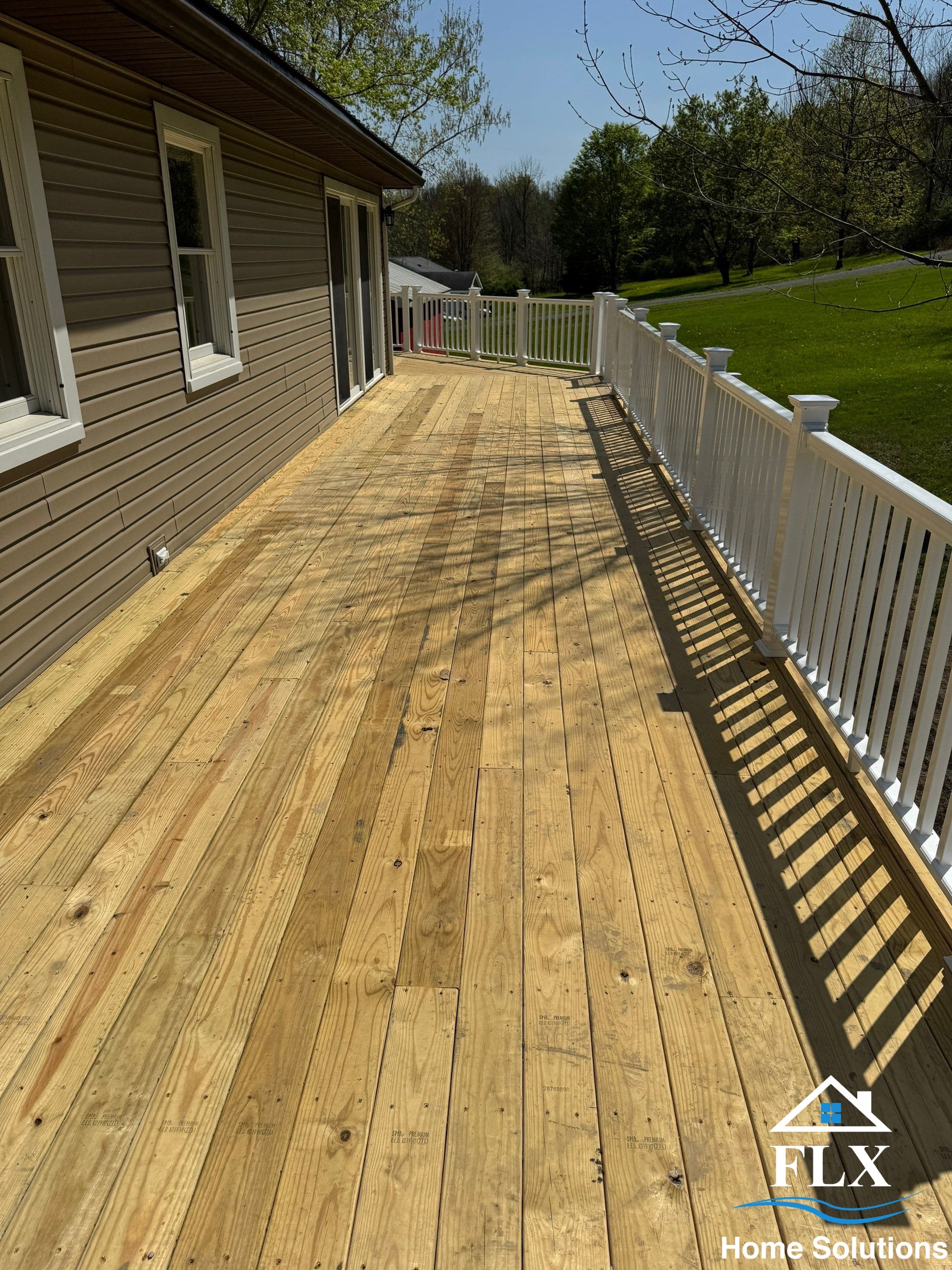 Natural wood deck with white railing and open yard view