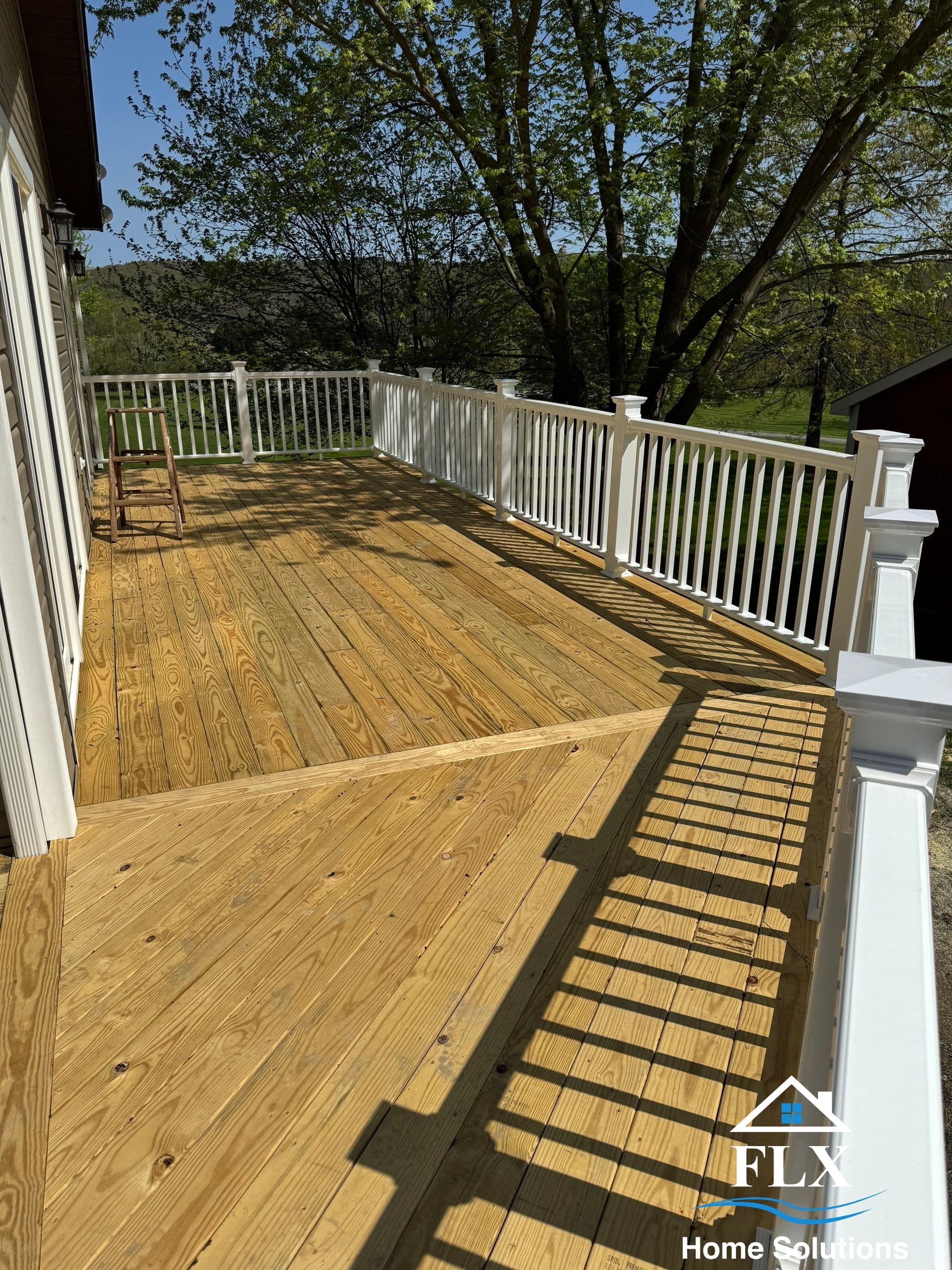 Natural wood deck with white railing and decorative posts overlooking trees
