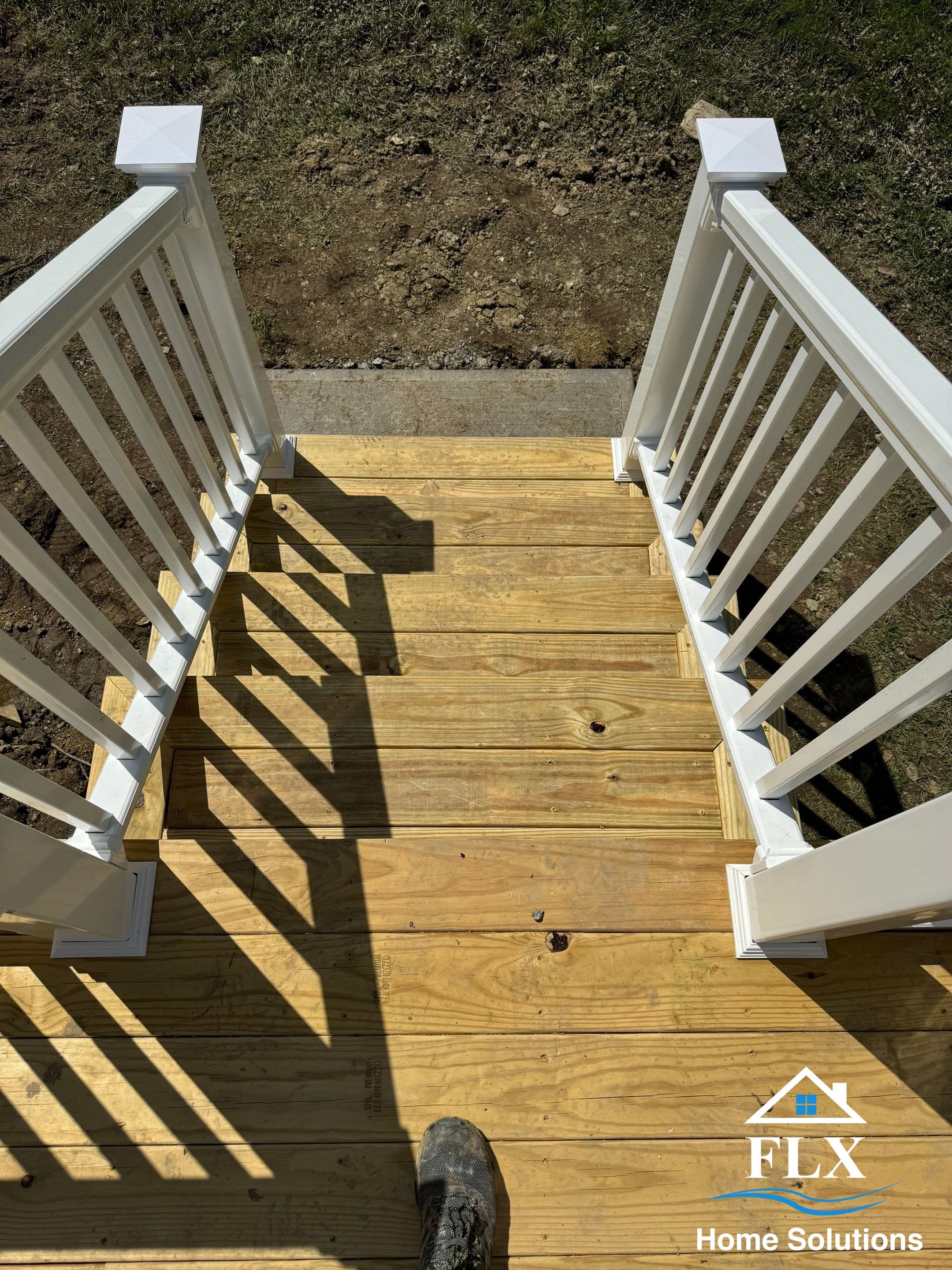 Wooden deck stairs with white railings leading down to bare ground