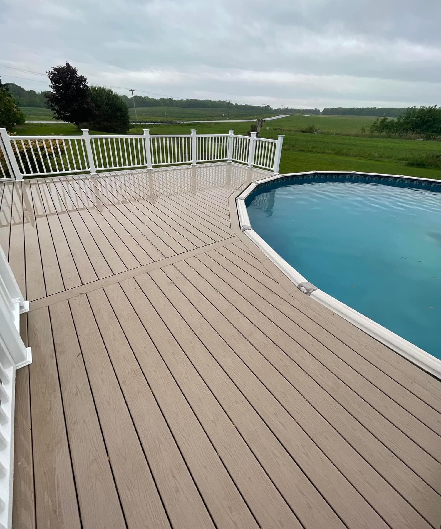 Tan composite deck with white railing surrounding above-ground pool