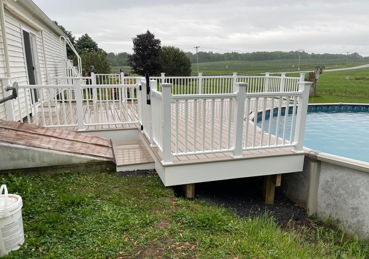 White composite deck with railings surrounding above-ground pool in rural backyard