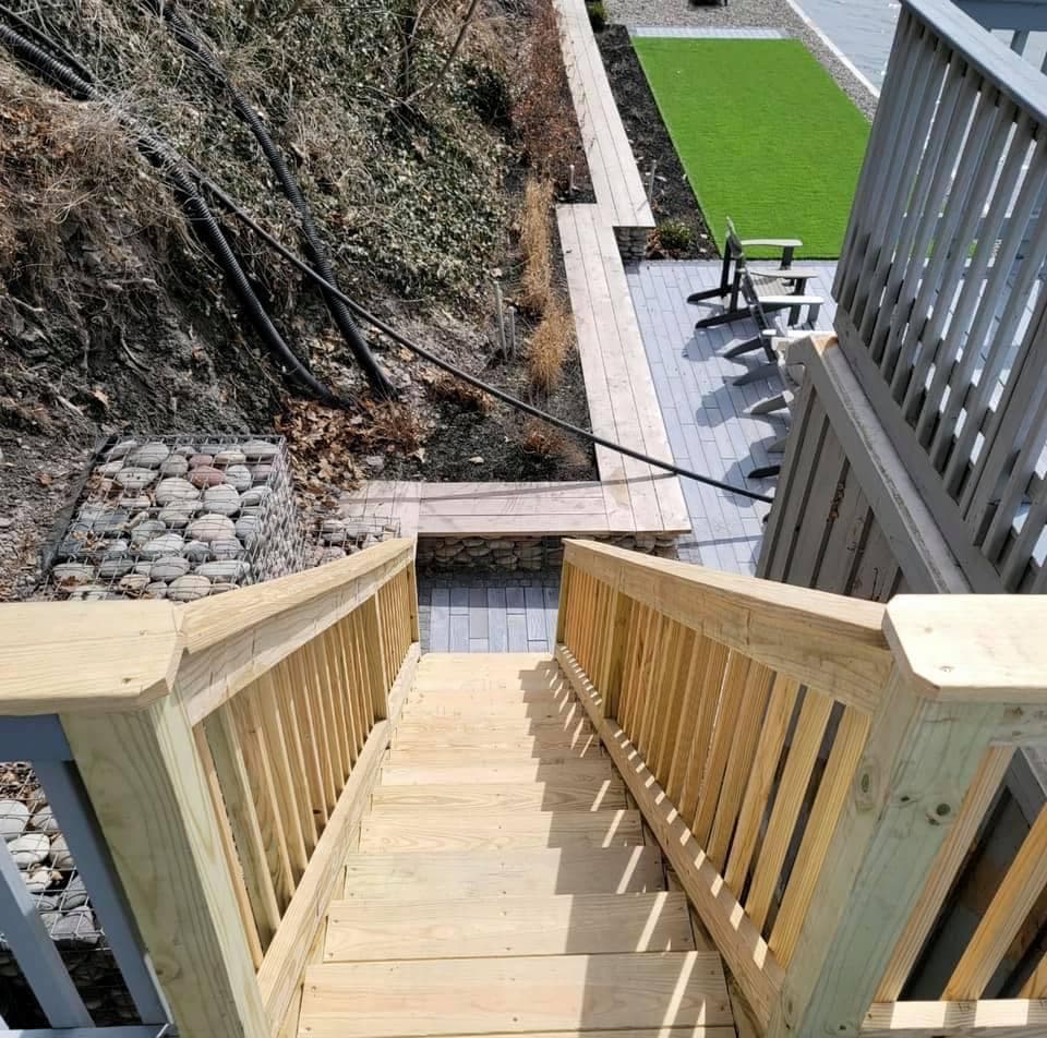 New wooden deck stairs leading down to paver patio with artificial turf lawn