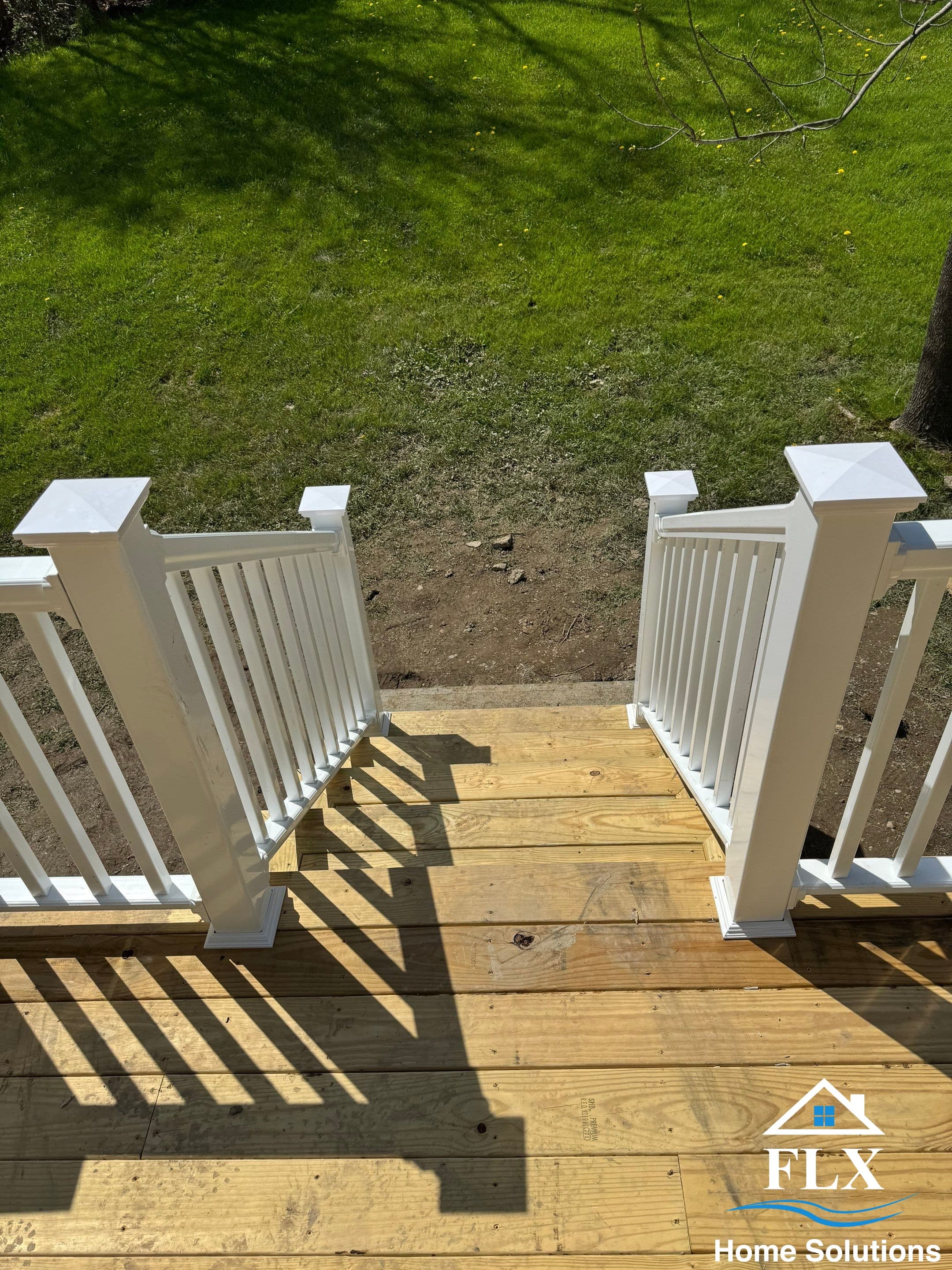 Wooden deck stairs with white vertical railings leading to backyard lawn