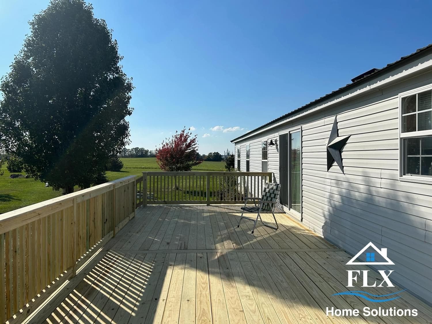 Wooden deck with railing overlooking green fields and trees under blue sky