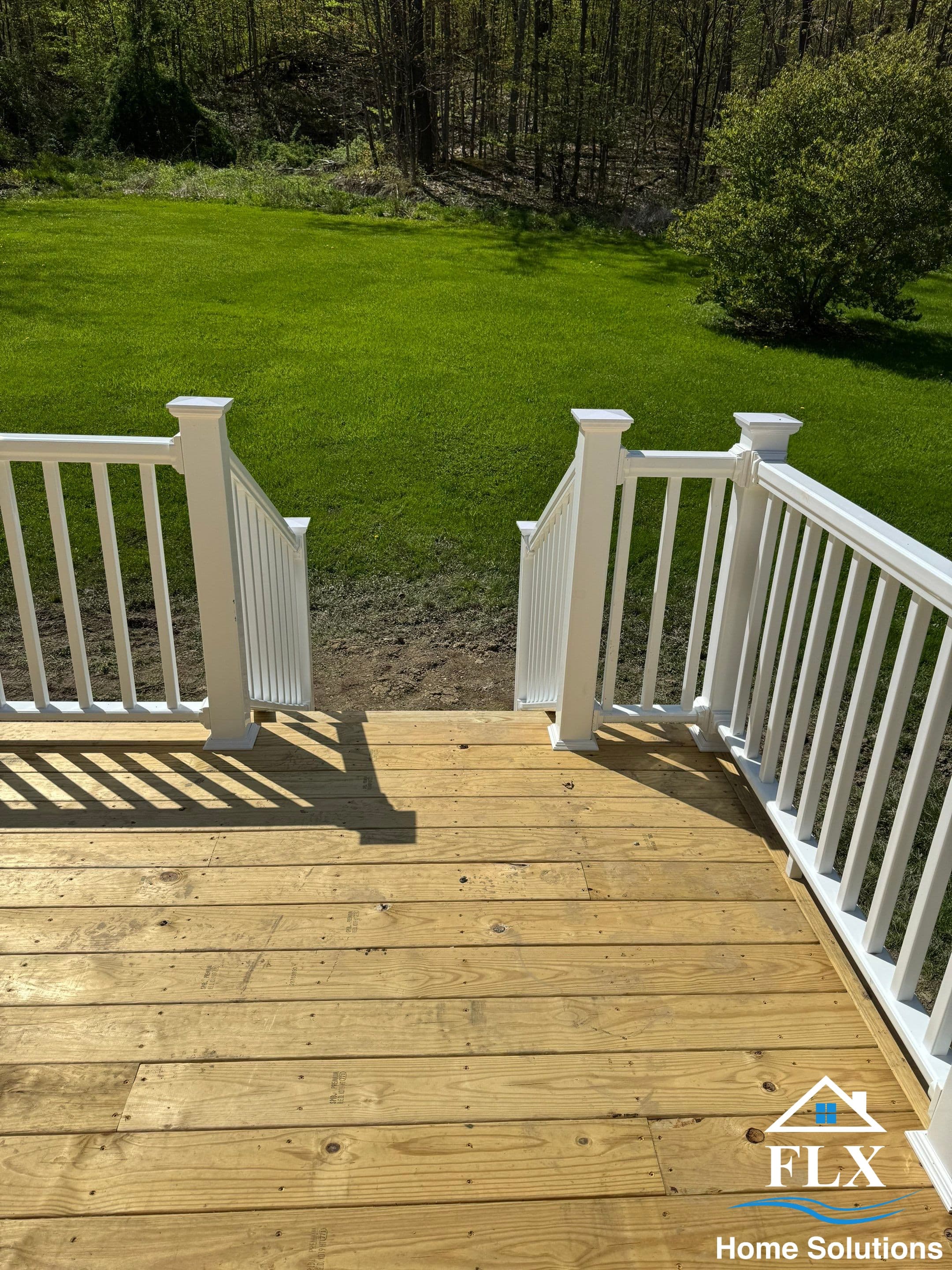 Wooden deck with white railings overlooking green lawn and wooded area