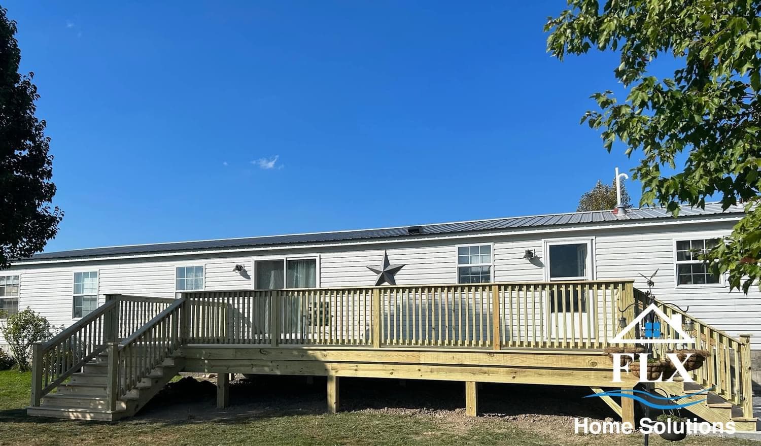 White mobile home with wraparound wooden deck featuring stairs and star decoration