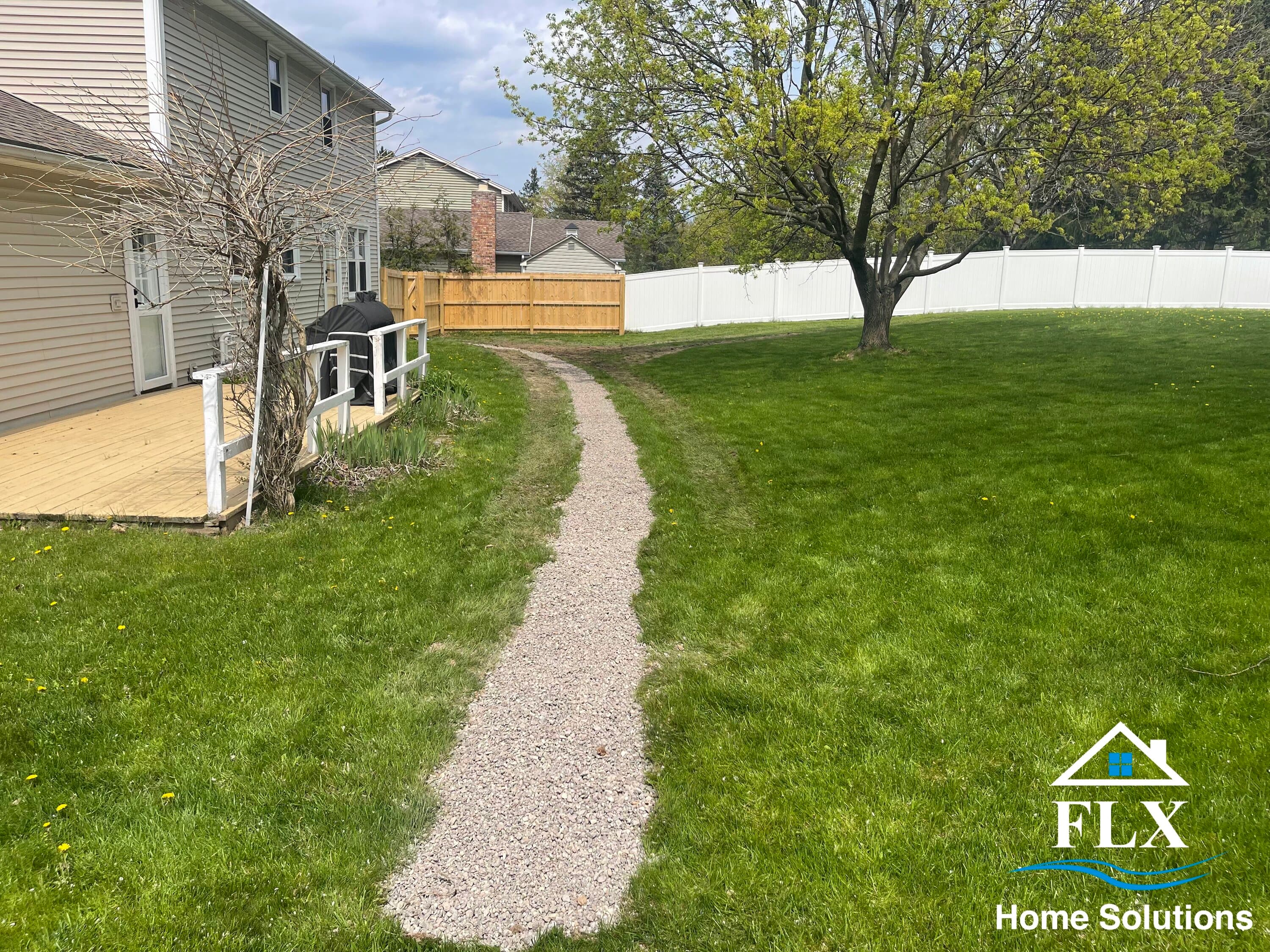 Gravel pathway leading through green lawn between wooden deck and tree