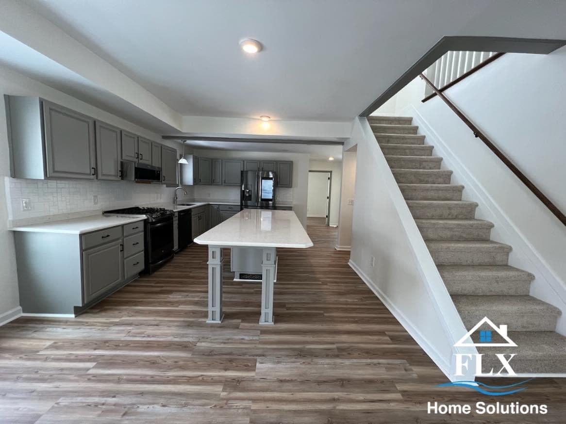 Open concept kitchen with gray cabinets, white island, and carpeted staircase