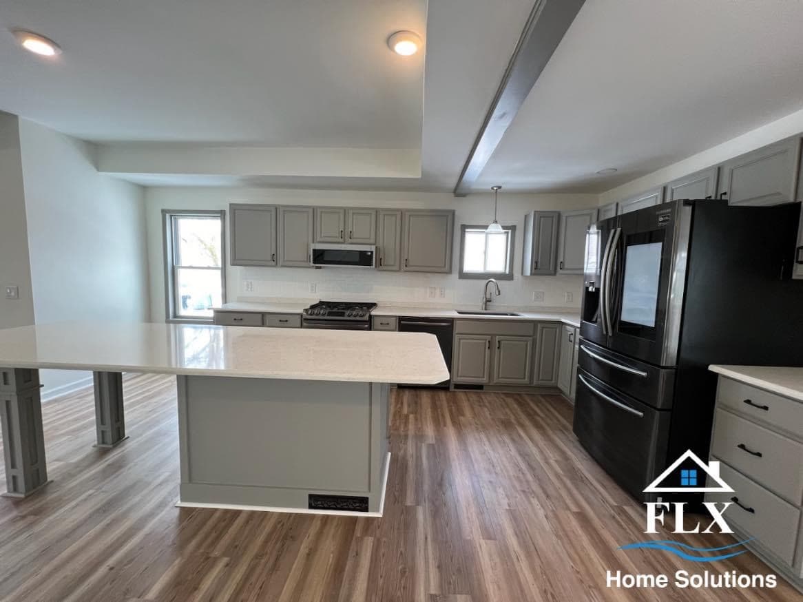 Modern open-concept kitchen with gray cabinets, white countertops, and wood-look flooring