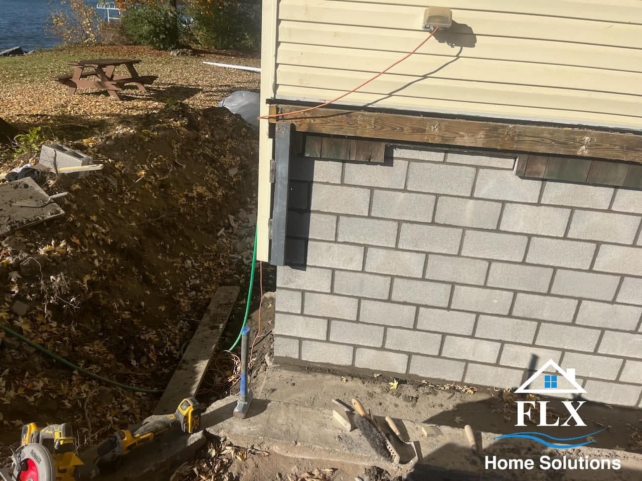 Concrete block foundation construction in progress with cream siding above