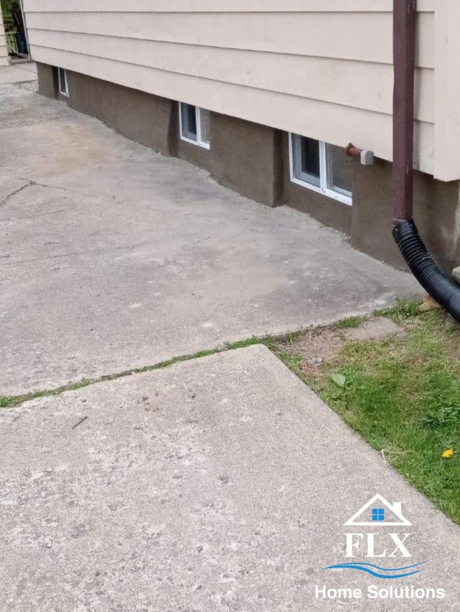 Concrete foundation with basement windows and downspout on house exterior