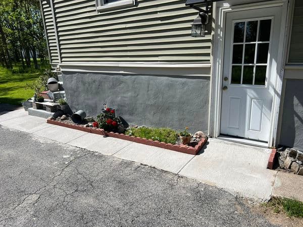 Concrete walkway leading to white door with brick flower bed and foundation
