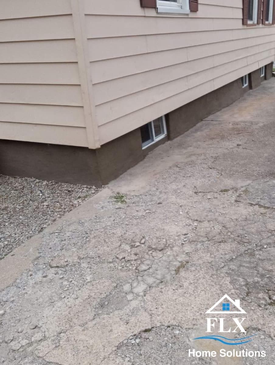 House foundation with beige siding, concrete base, and basement windows