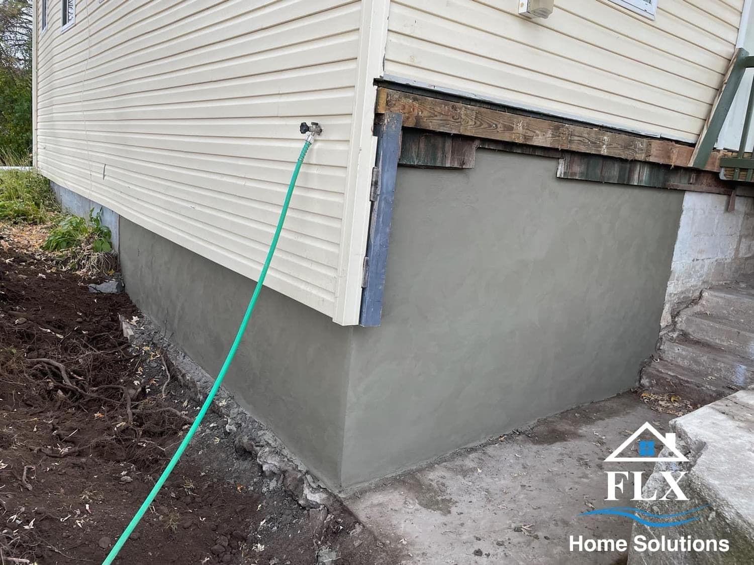 Freshly poured concrete foundation repair on house with beige vinyl siding