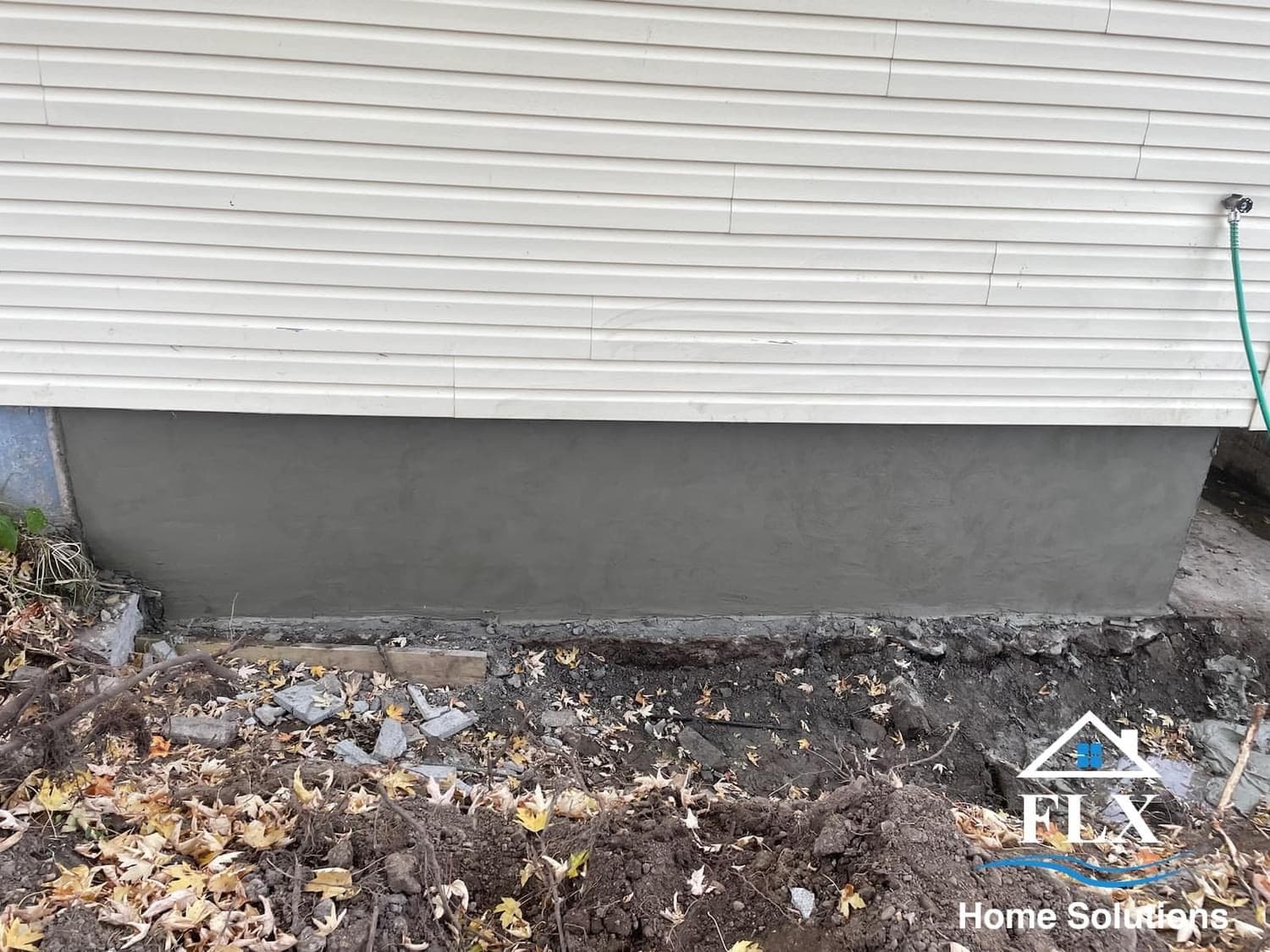 Newly poured concrete foundation repair at base of white vinyl siding