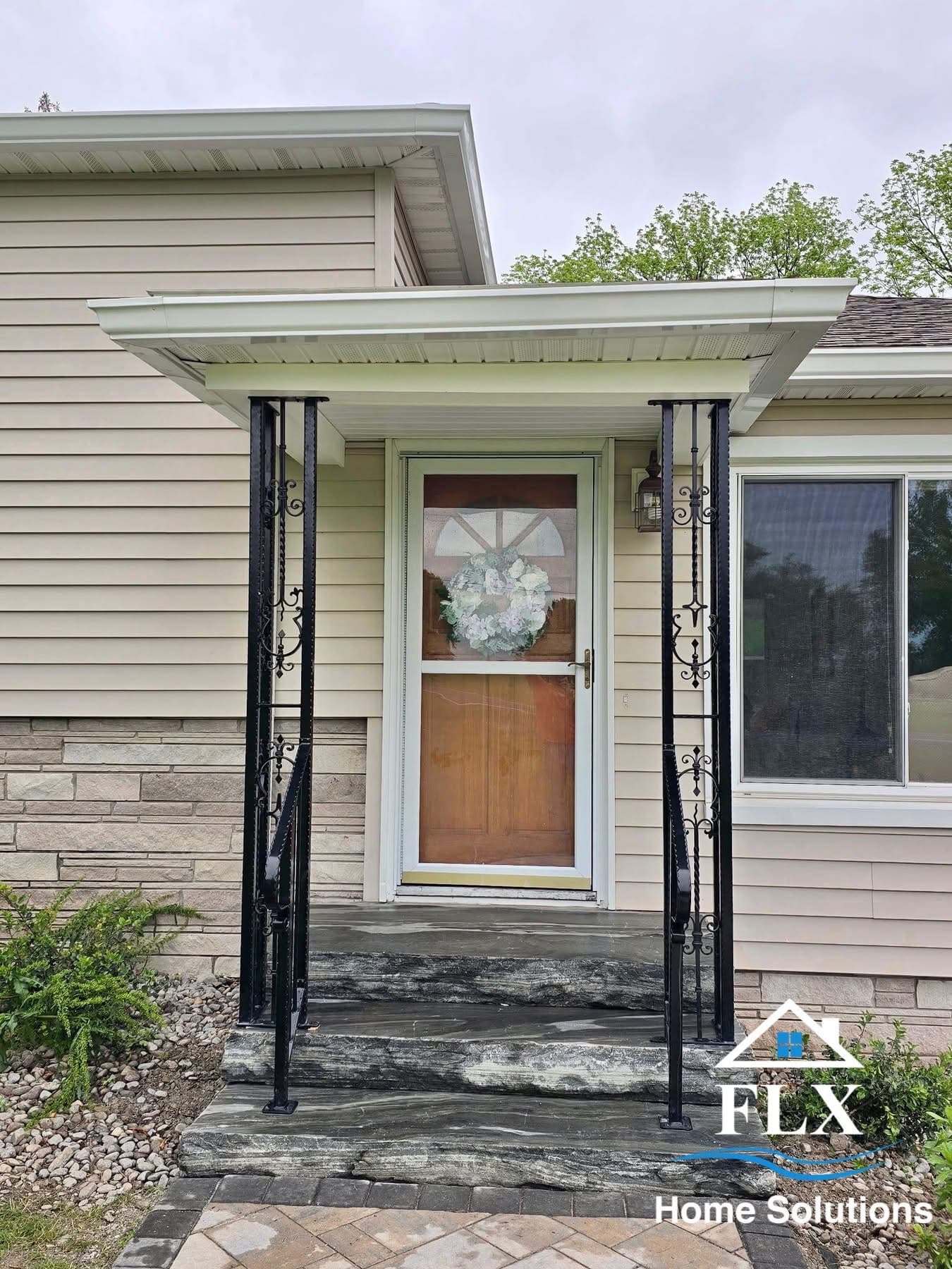 Covered front porch entry with decorative black metal railings and wreath